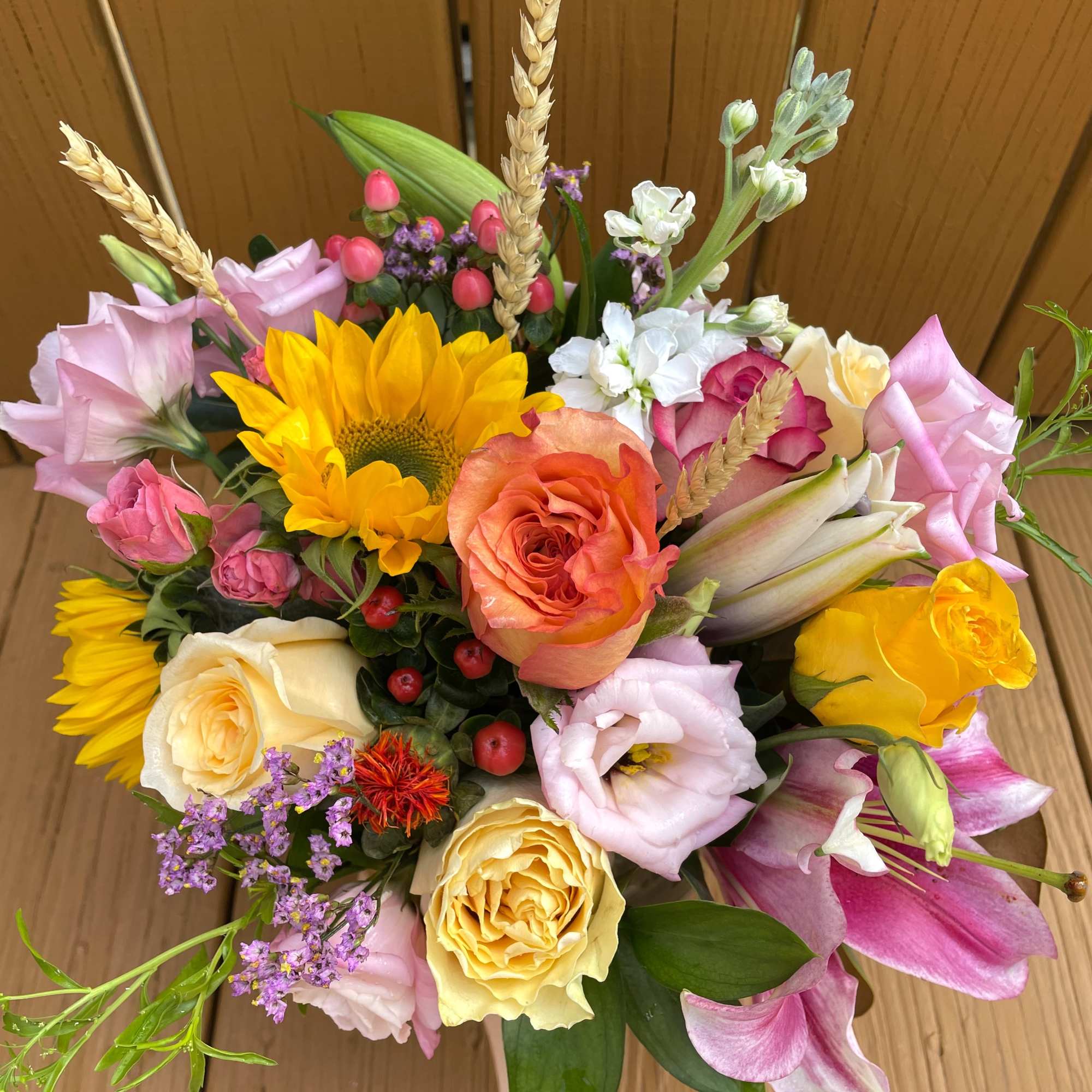 Vibrant mixed bouquet with sunflowers, roses, lilies, and lisianthus in a low container