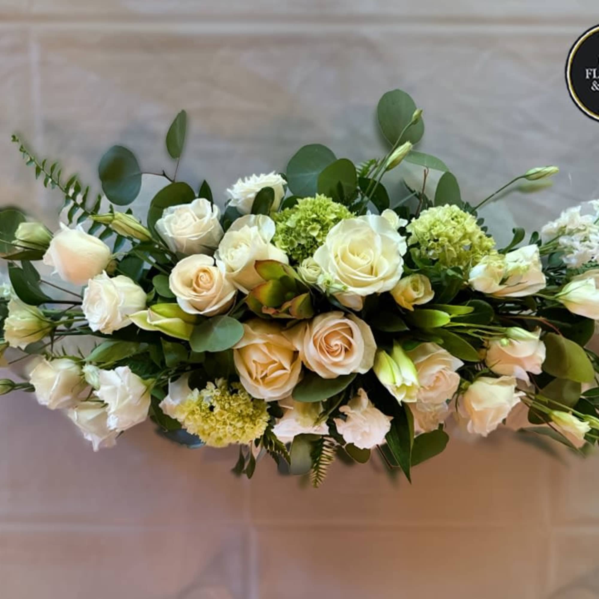 Long low arrangement of white and cream roses with green accents styled as an elegant centerpiece