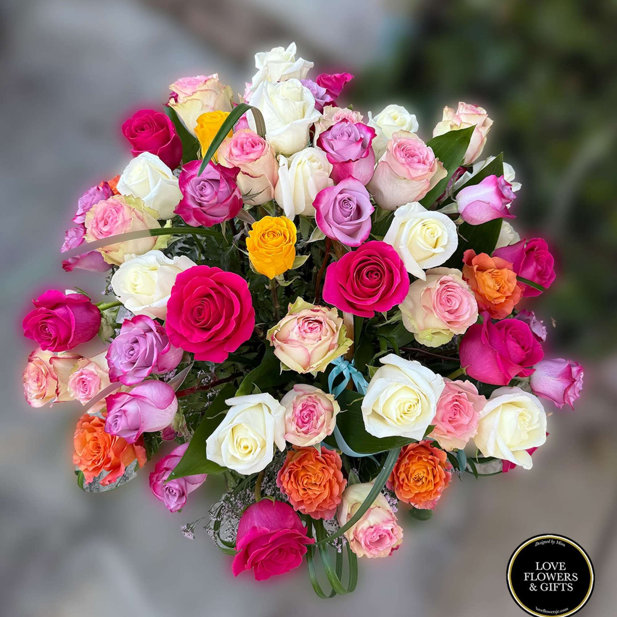Large round bouquet of mixed pink, white, orange, yellow, and lavender roses viewed from above