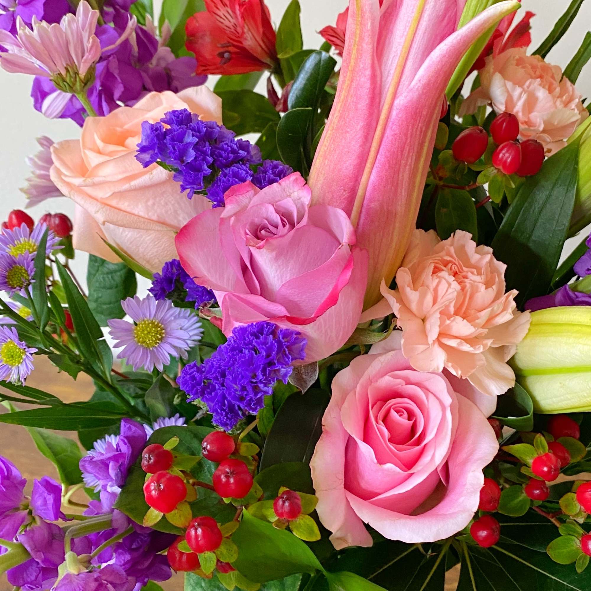 Mixed bouquet of pink roses, lilies, and peach carnations with purple blooms and red berries