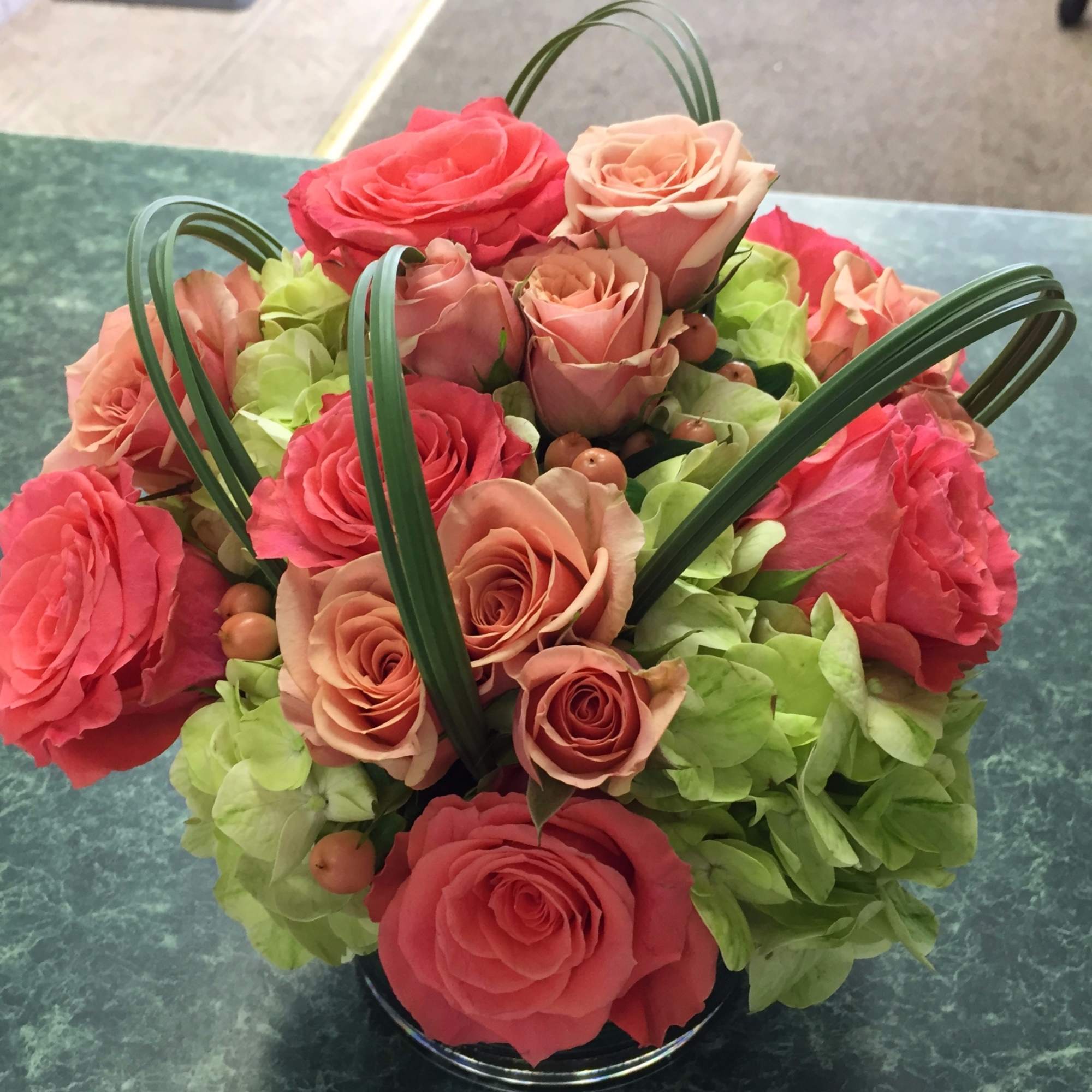Pink and peach roses arranged with green hydrangeas in a round vase