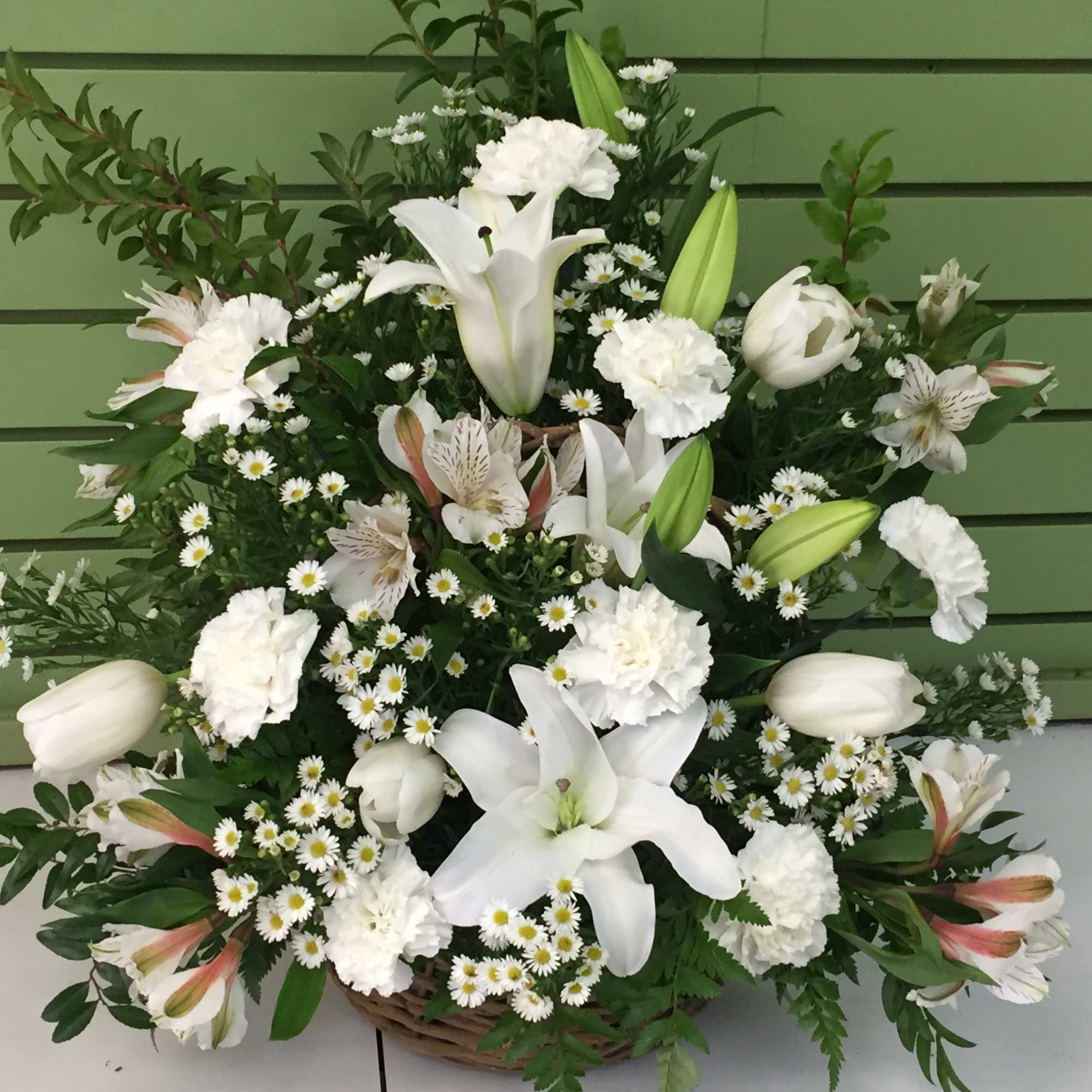 White lilies, carnations, and small daisy flowers arranged in a basket