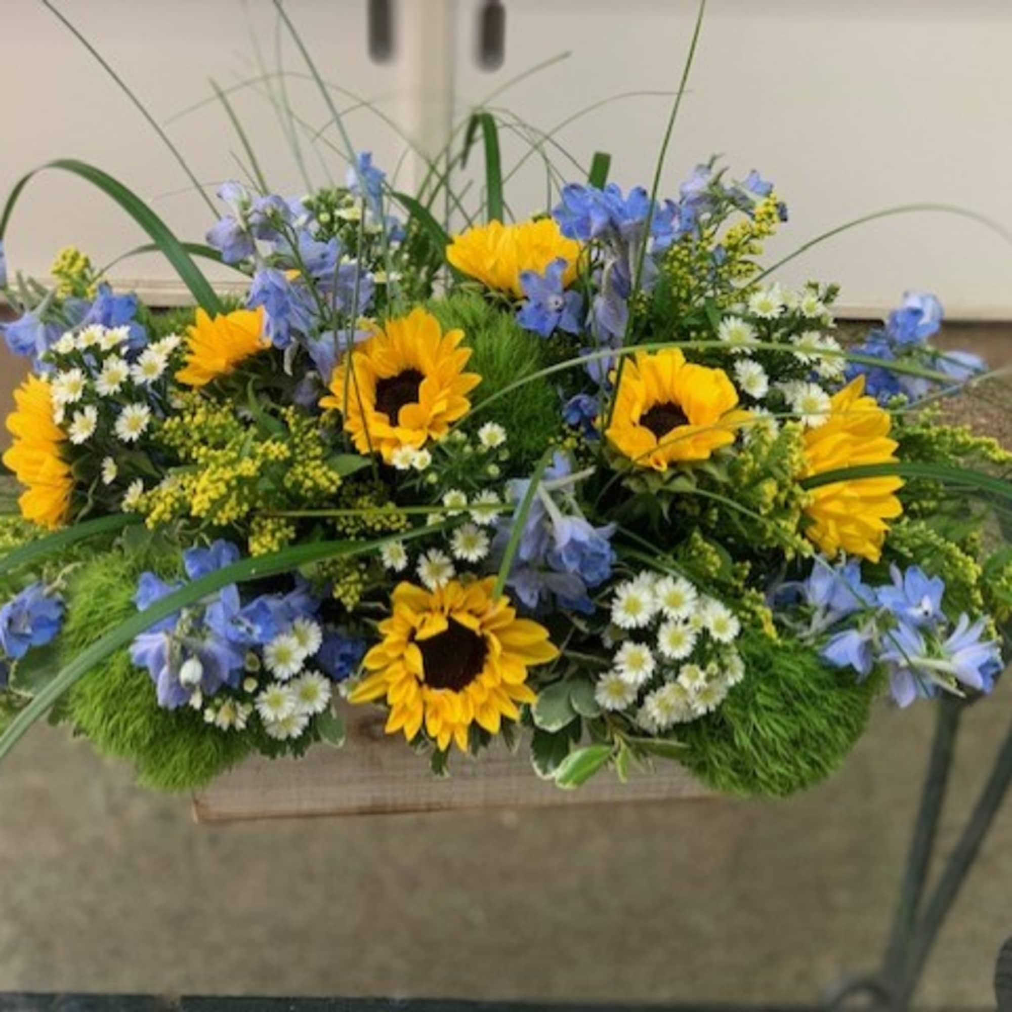 Low floral arrangement with yellow sunflowers and blue flowers in a rectangular container