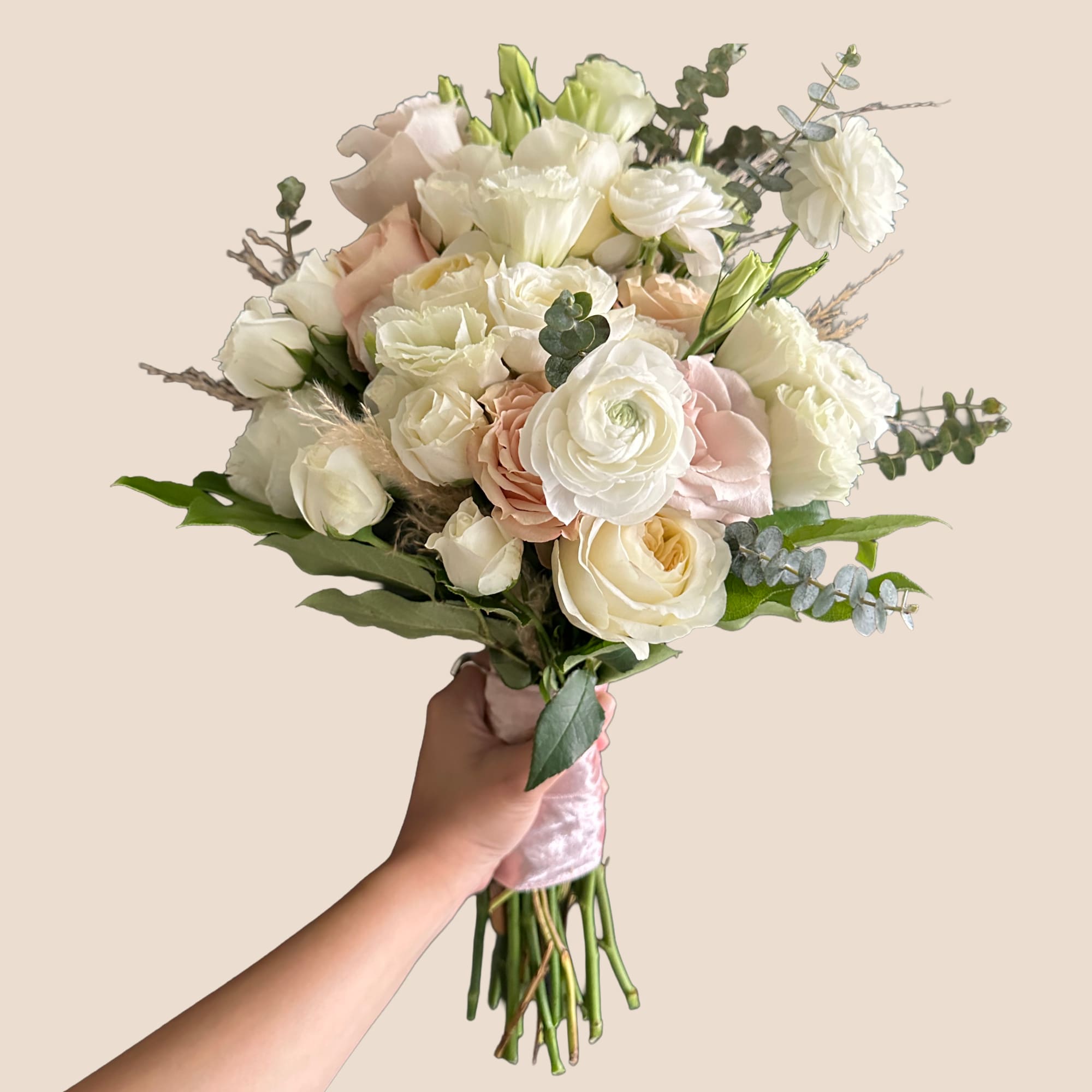 Handheld bouquet of white and blush flowers with pink ribbon wrap