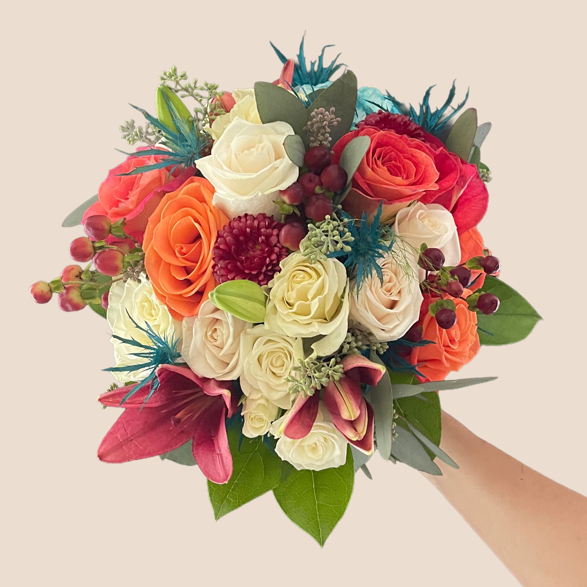 Handheld bouquet of roses in orange, white, and pink with magenta lilies