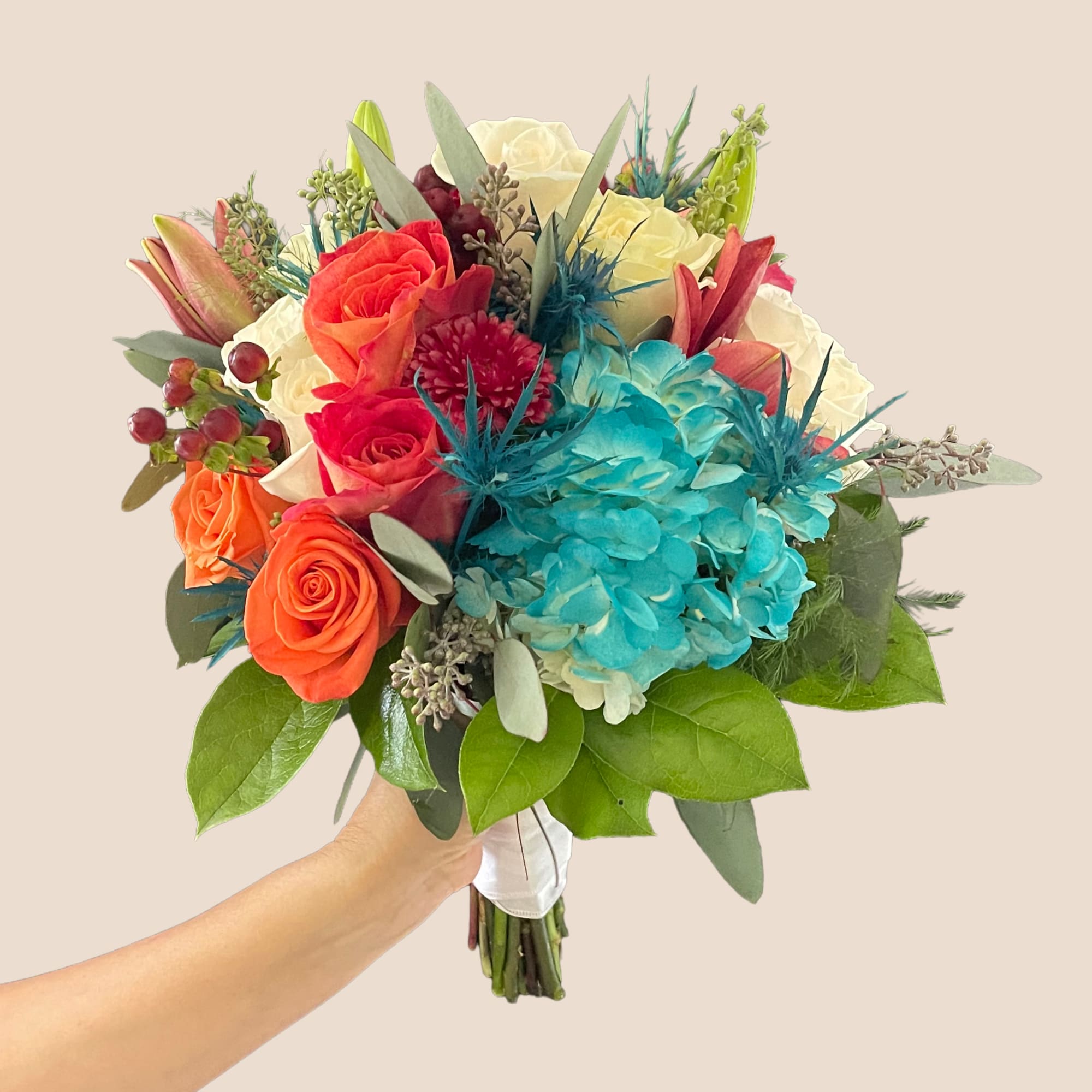 Handheld bouquet of roses, hydrangeas, and lilies in bright mixed colors