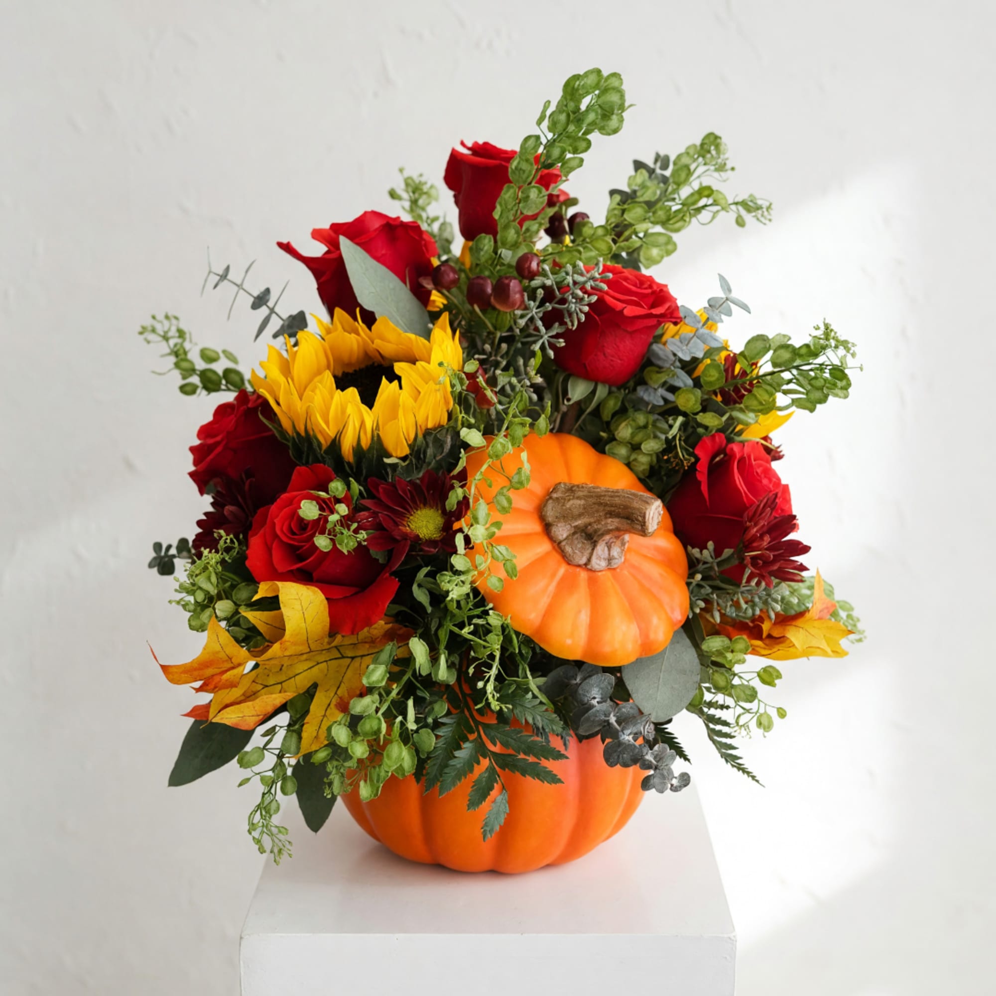 Fall floral arrangement in a pumpkin container with red roses and yellow blooms