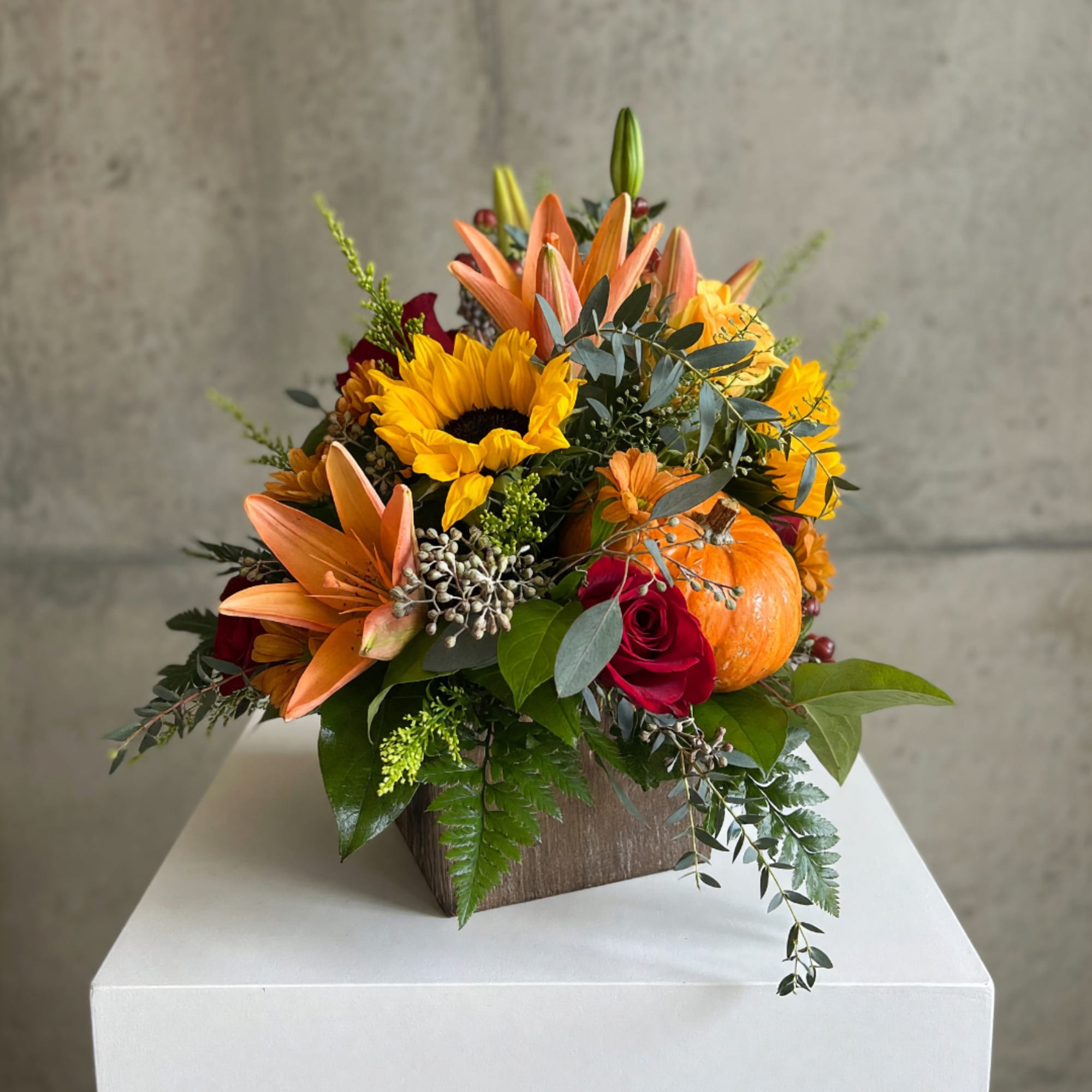 Autumn floral arrangement with sunflowers, lilies, roses, and a pumpkin in a wooden box