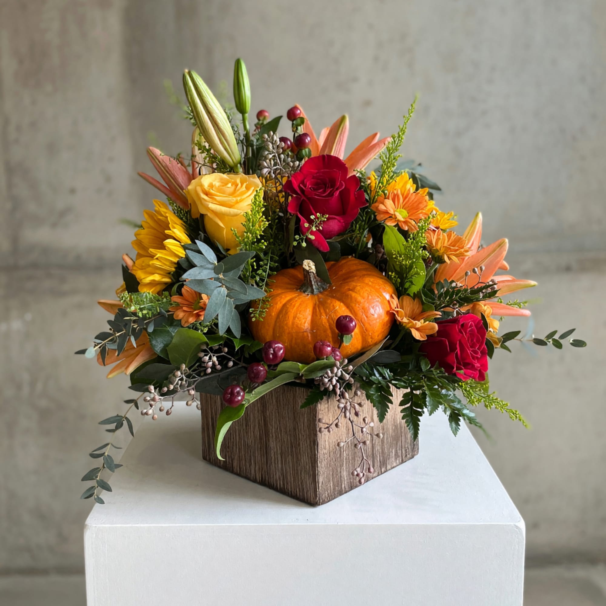 Autumn floral arrangement with roses, lilies, and a pumpkin in a wooden box