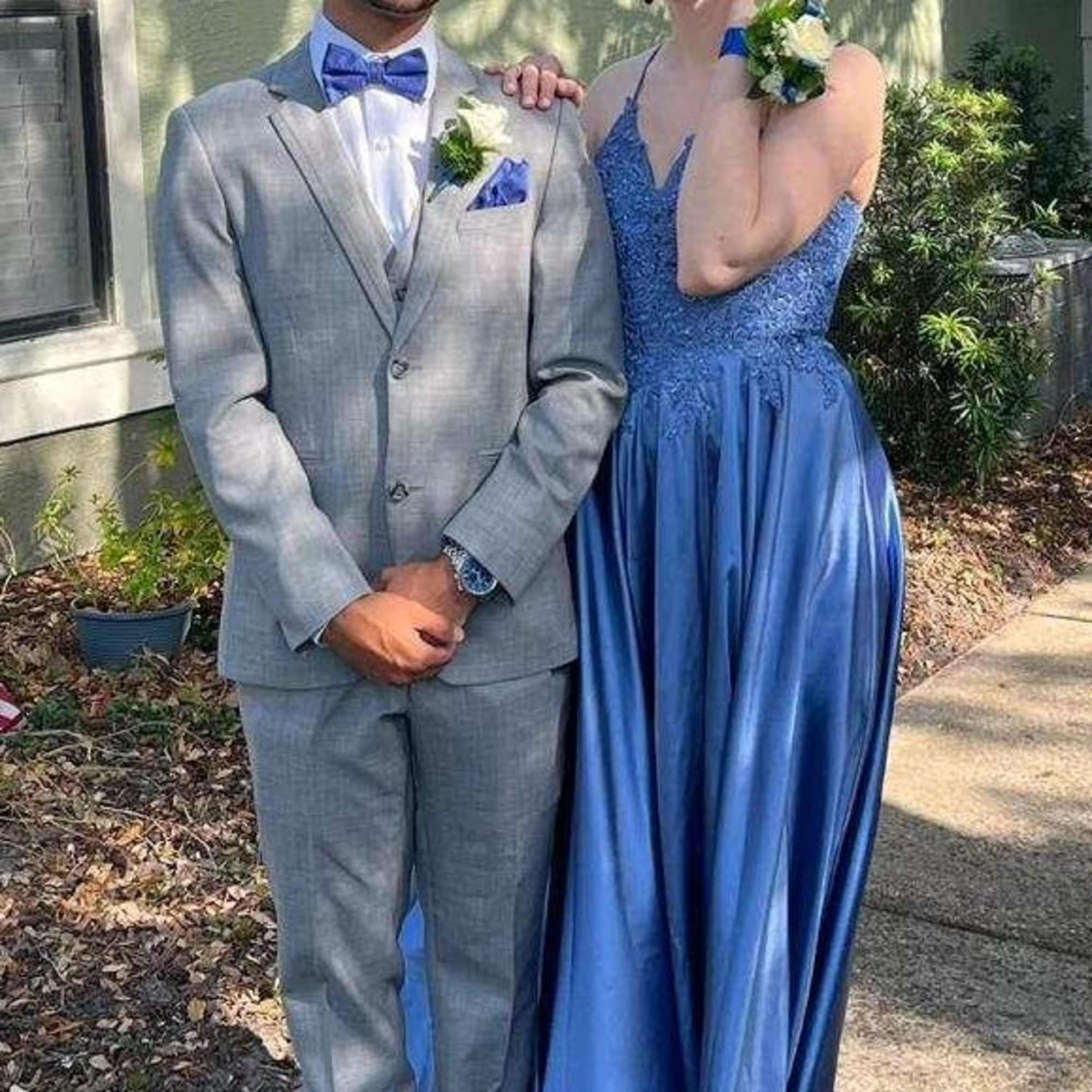 White rose wrist corsage and matching boutonniere with blue ribbon worn by a dressed-up couple.