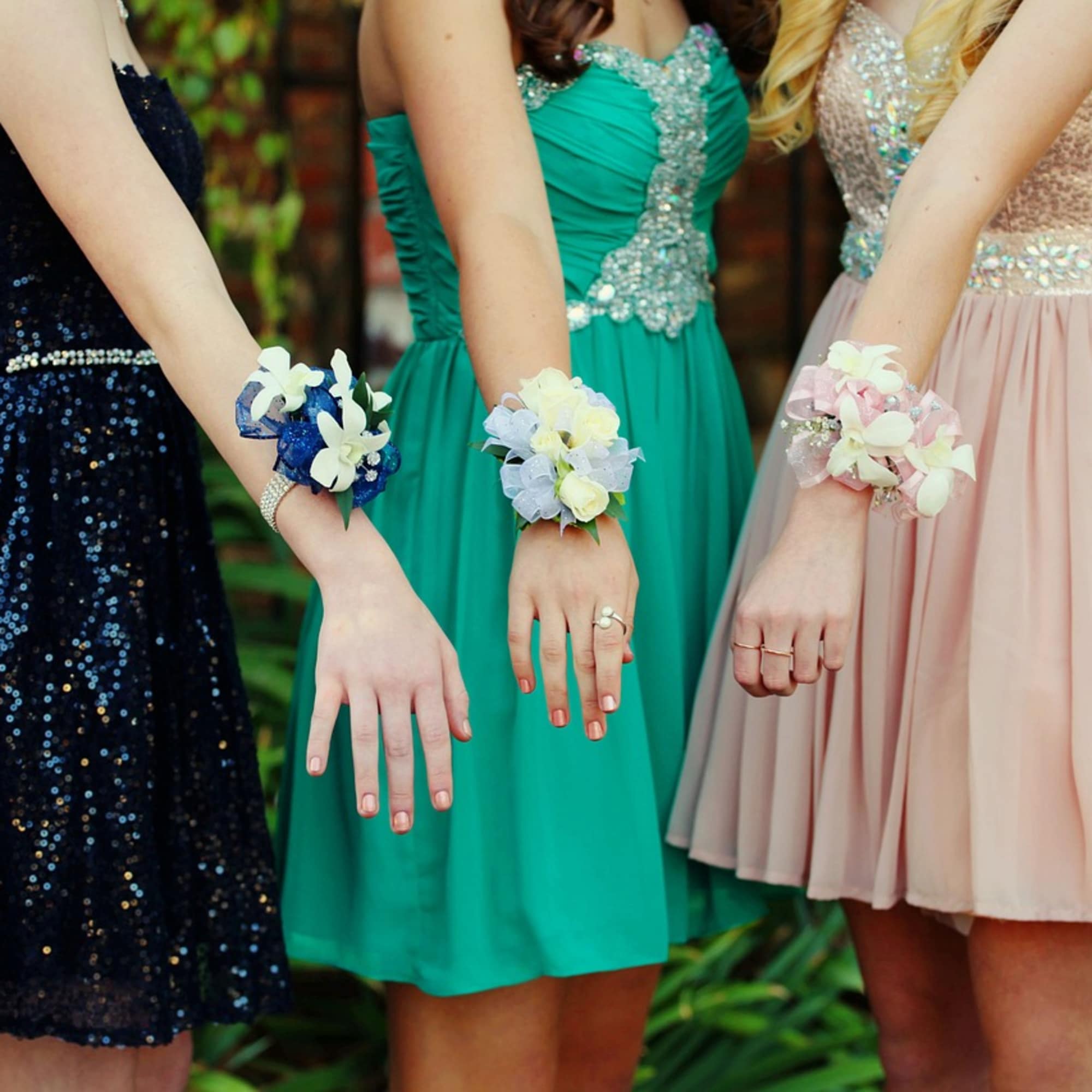 Three wrist corsages with white and pastel flowers worn with formal dresses.