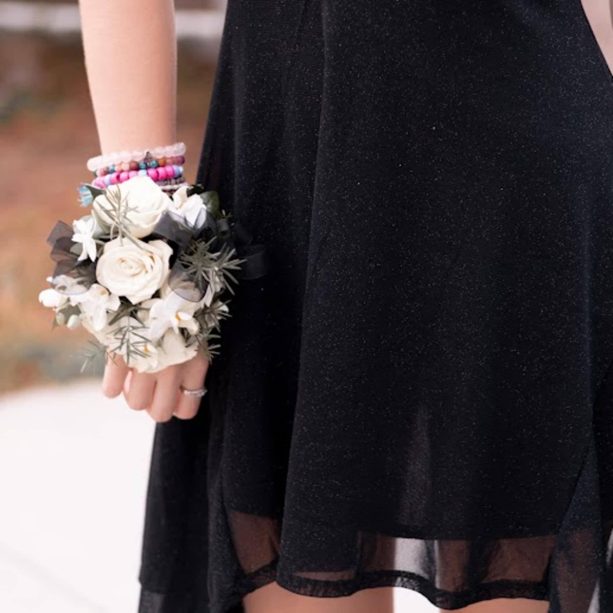 White rose wrist corsage with black ribbon worn with a black dress