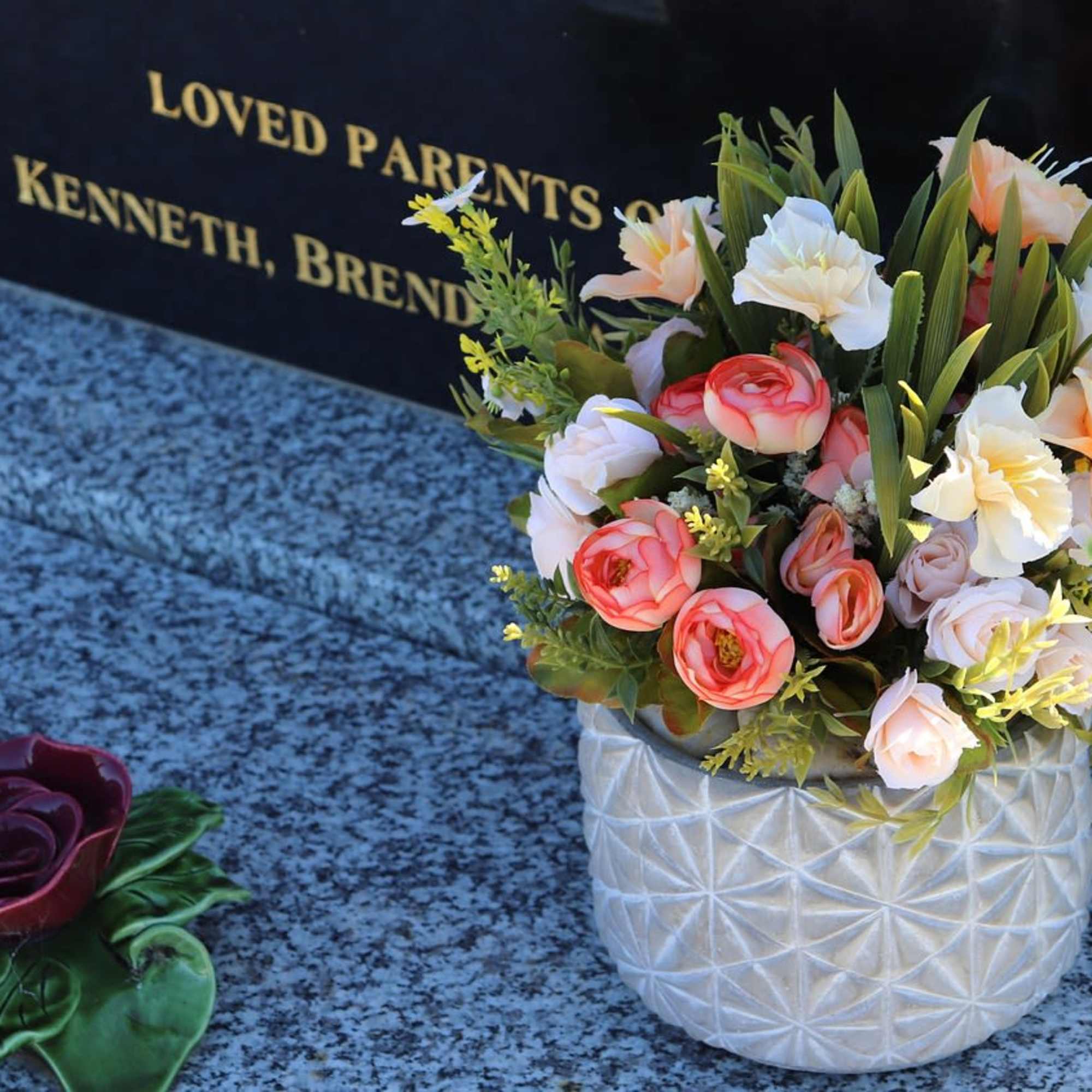 Mixed bouquet in a white textured vase beside a memorial plaque
