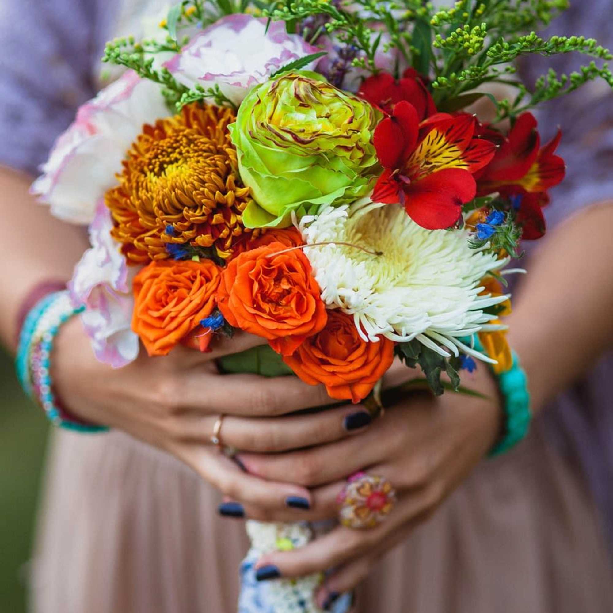 Handheld bouquet of mixed orange, red, white, and green flowers