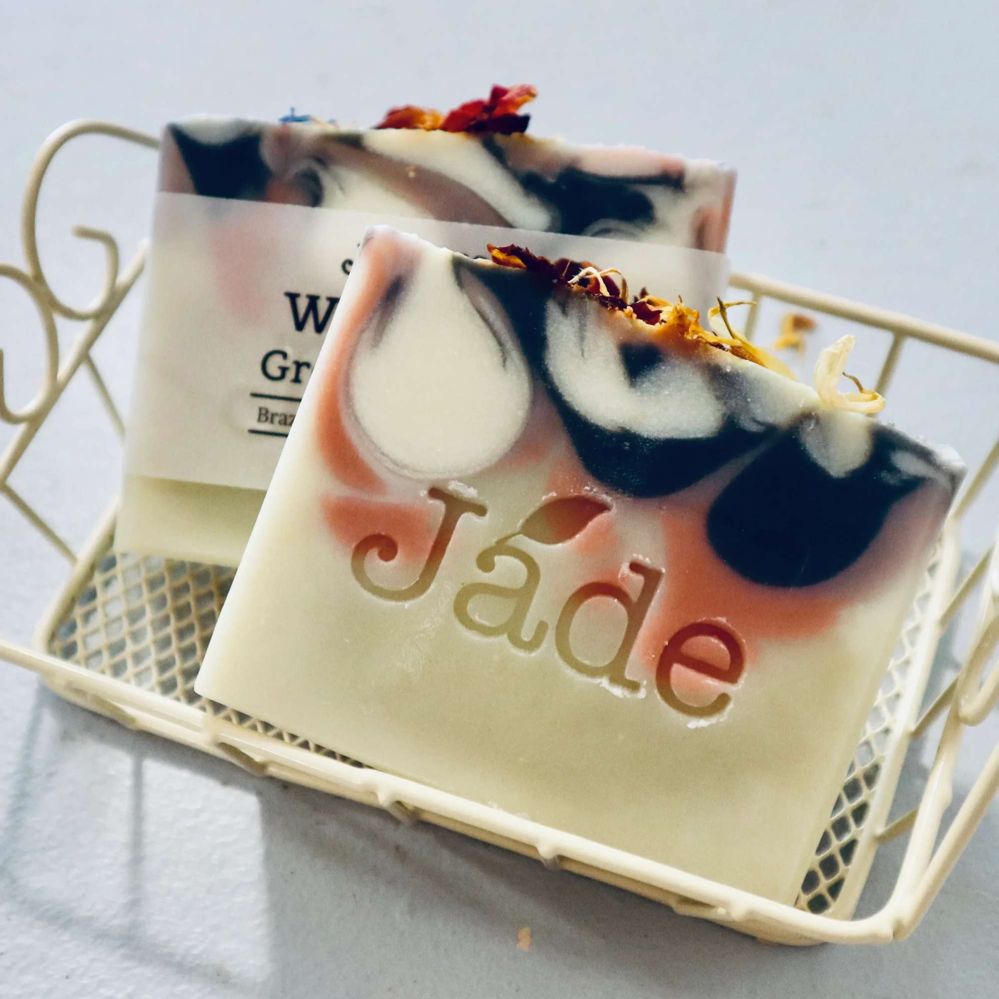 Two decorative soap bars with pink and black swirls in a small cream metal basket