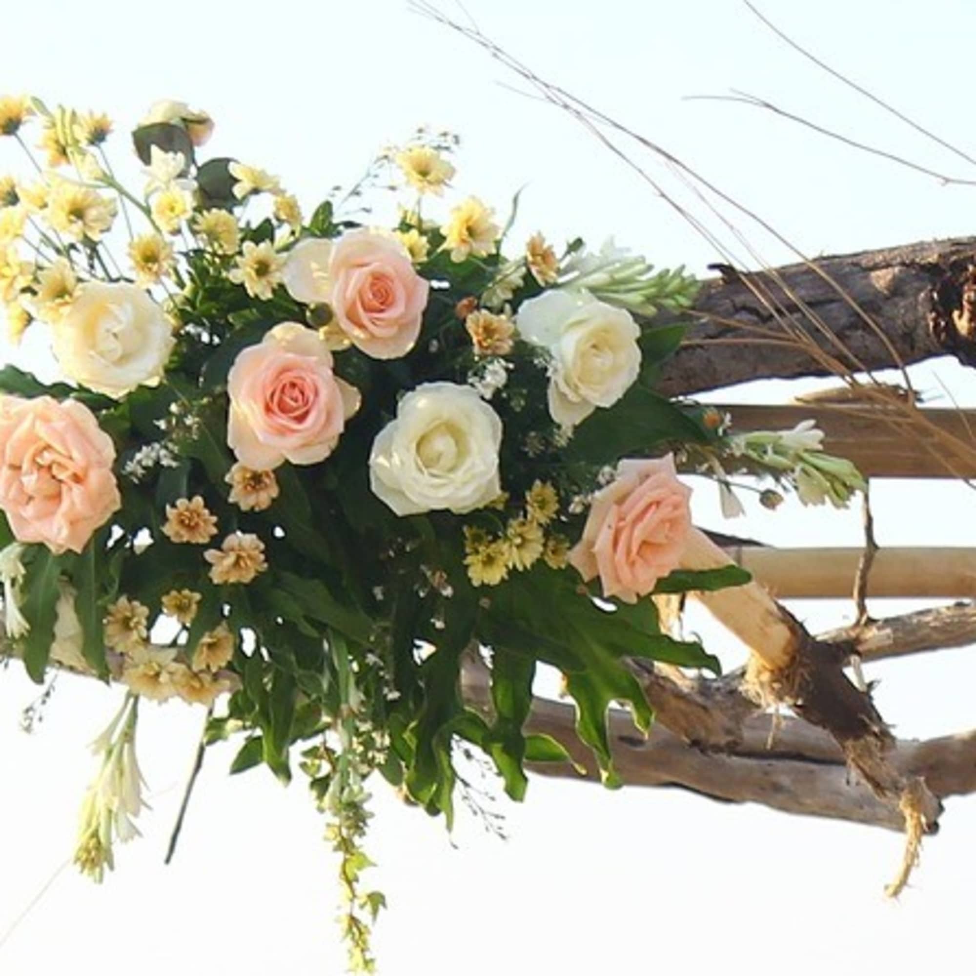 Floral arrangements of peach and white roses hang from a rustic wooden arch.