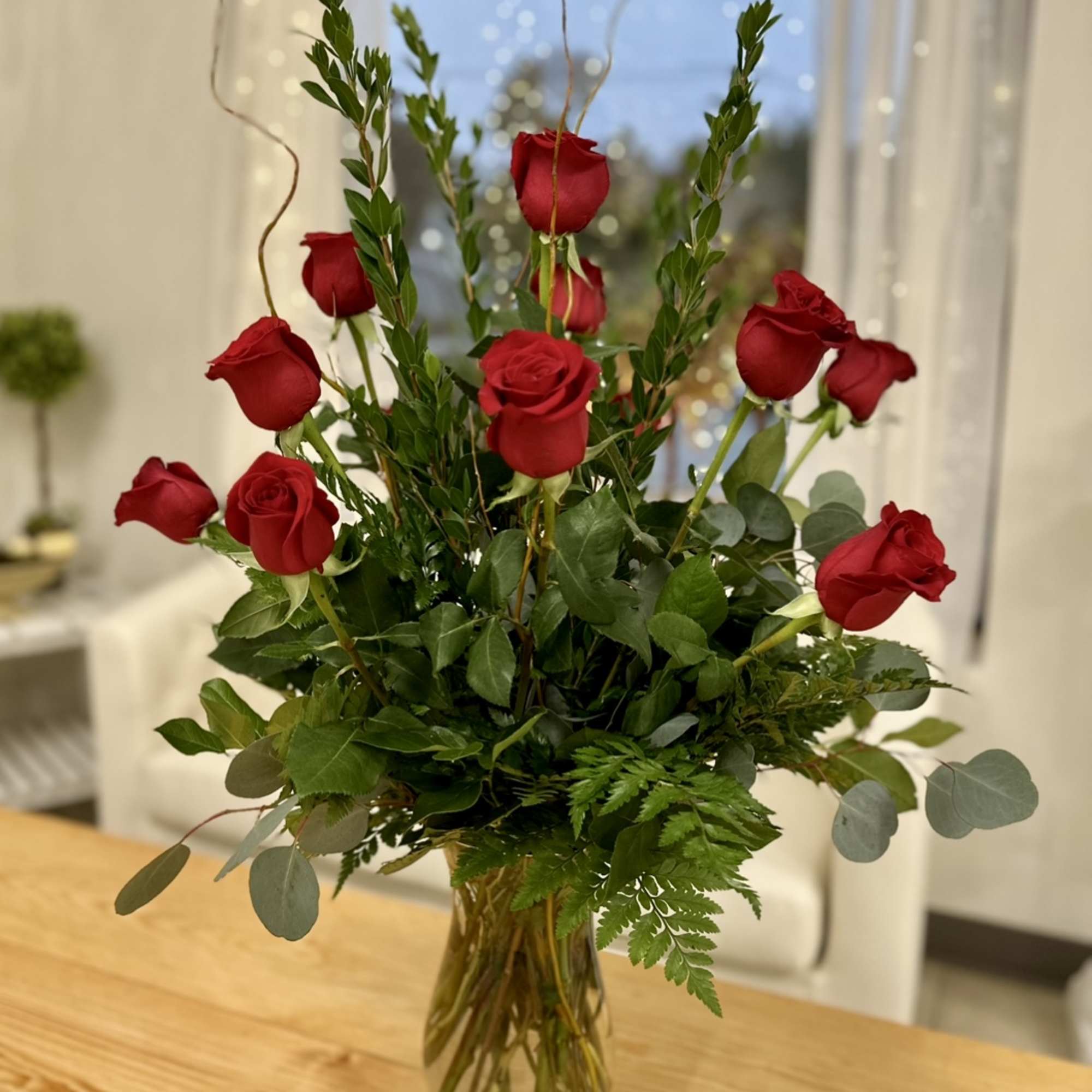 Red roses arranged in a clear glass vase with mixed greenery
