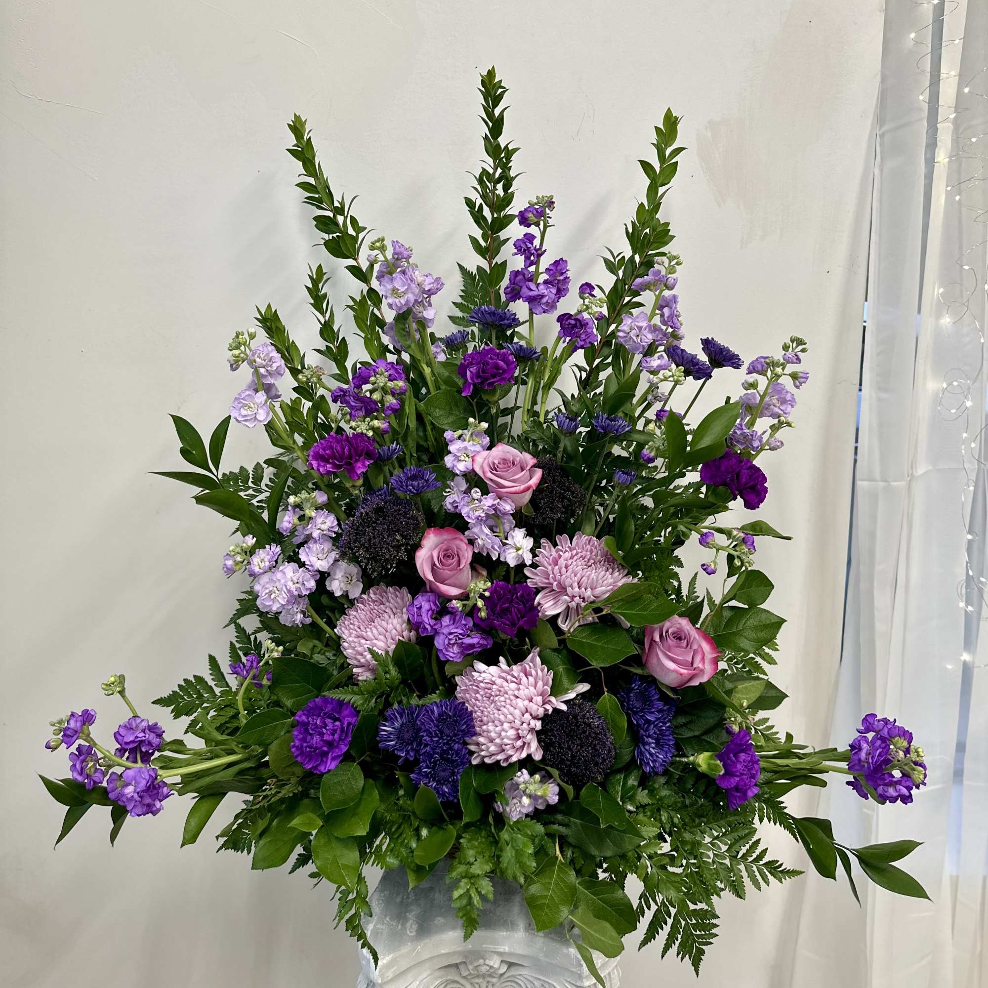 Tall purple and pink floral arrangement in a white pedestal vase