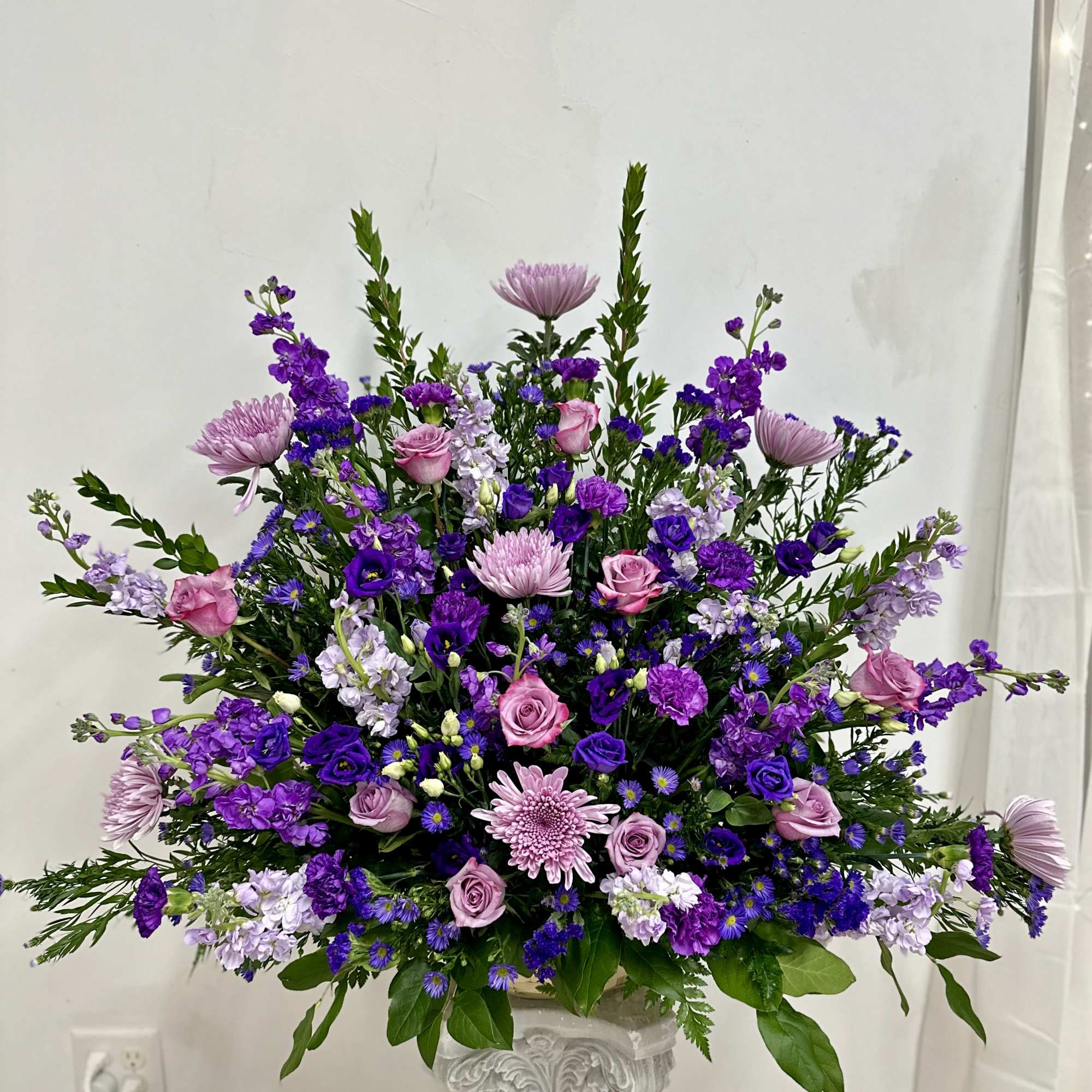 Large purple and pink floral arrangement in a white pedestal vase