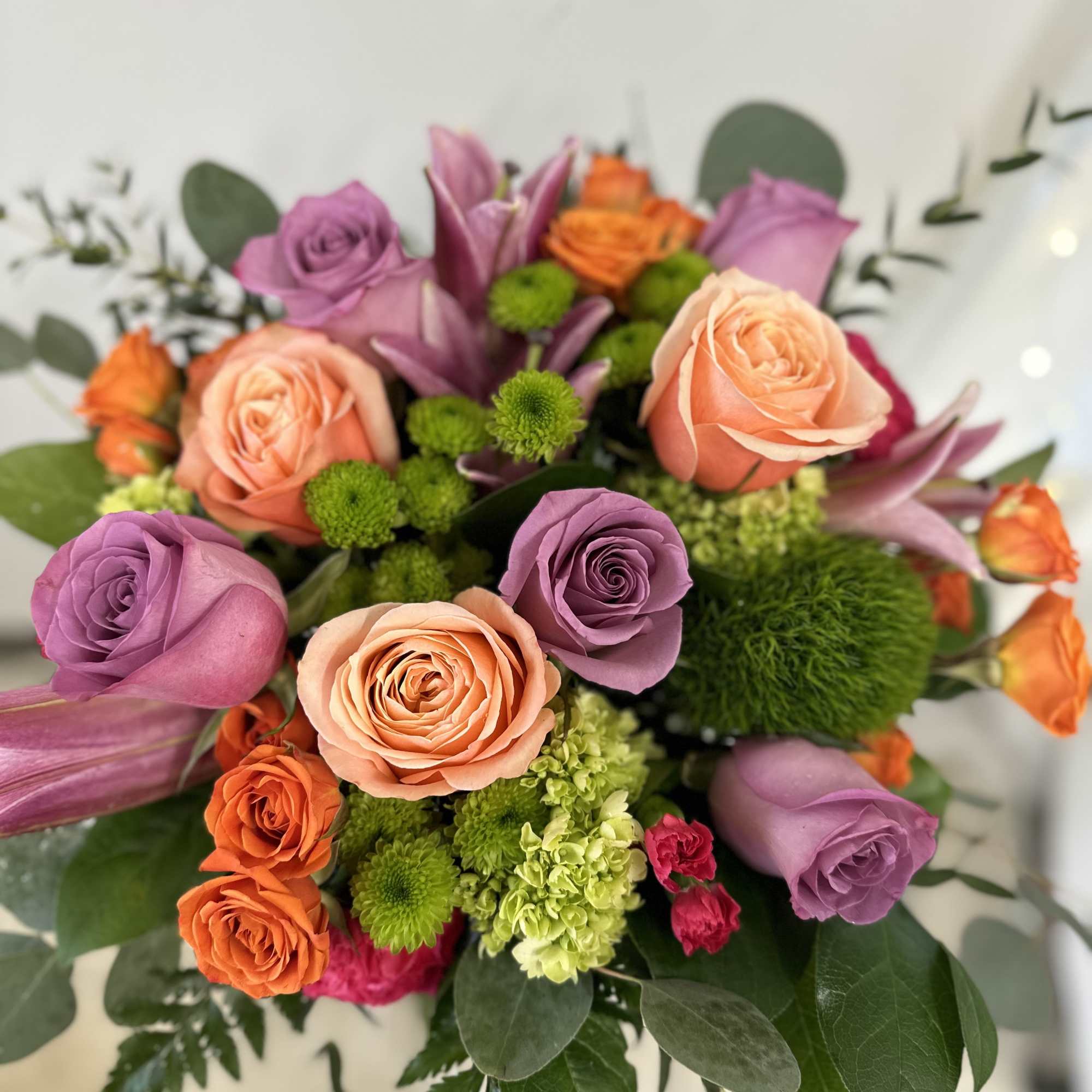 Bouquet of peach, lavender, and orange roses with green accents