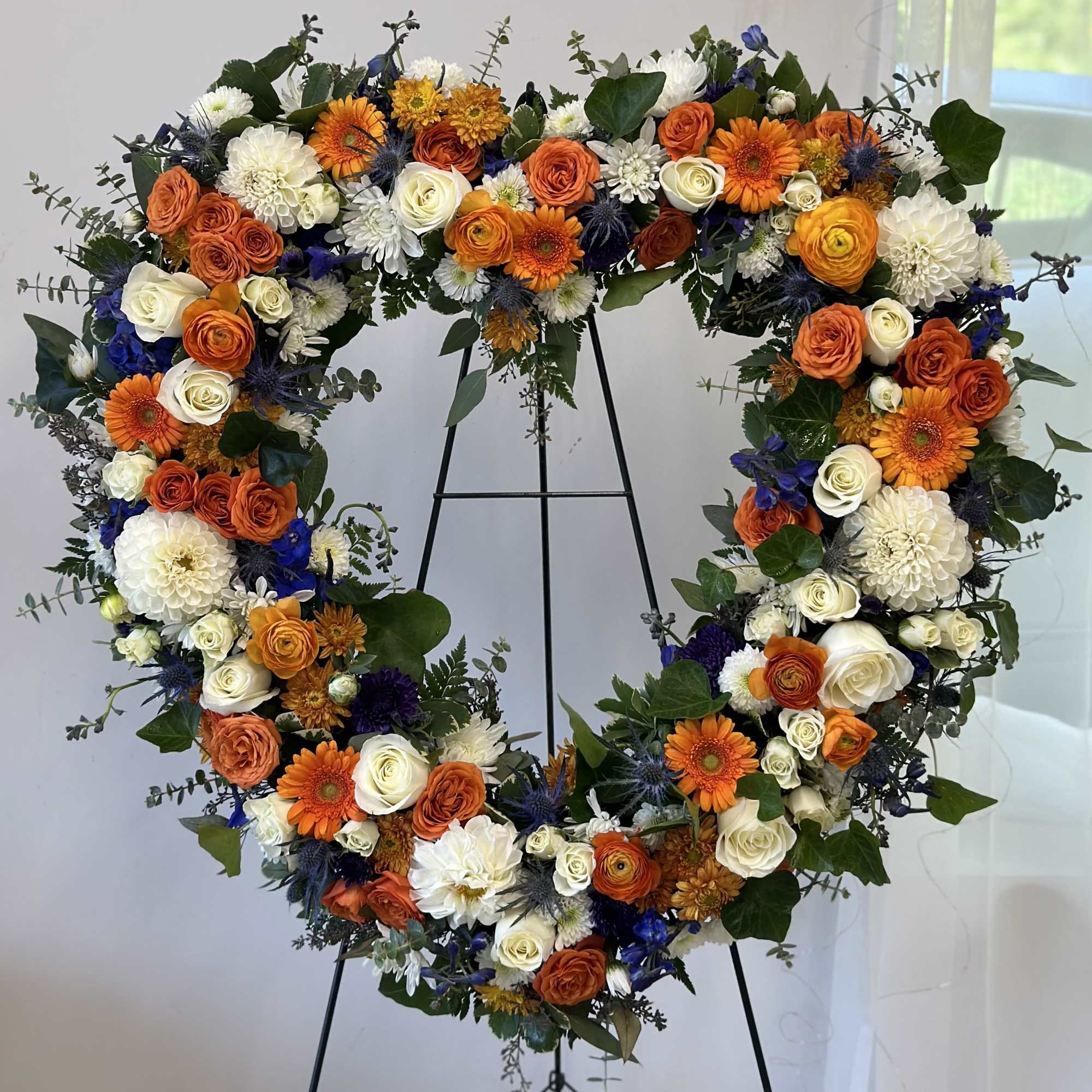Heart-shaped floral wreath with orange, white, and blue flowers on a stand, photo 2 of 2