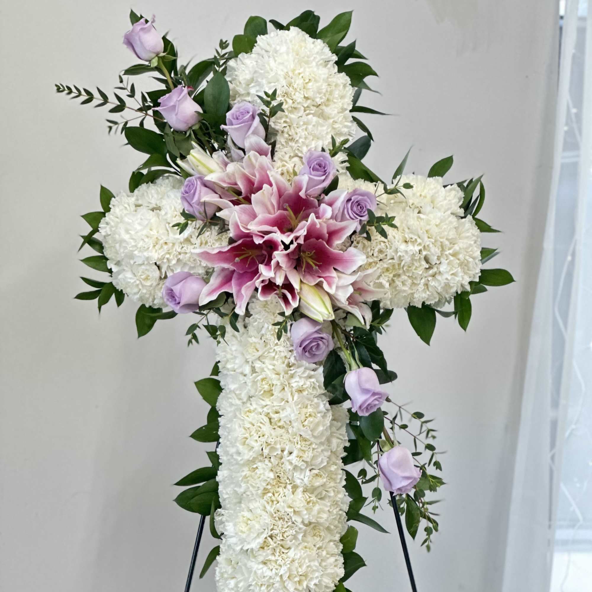 White floral cross with pink lilies and lavender roses on an easel