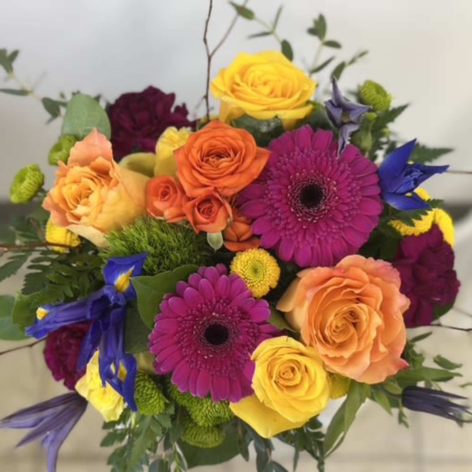Vibrant bouquet of pink gerbera daisies, yellow and orange roses, and blue irises.