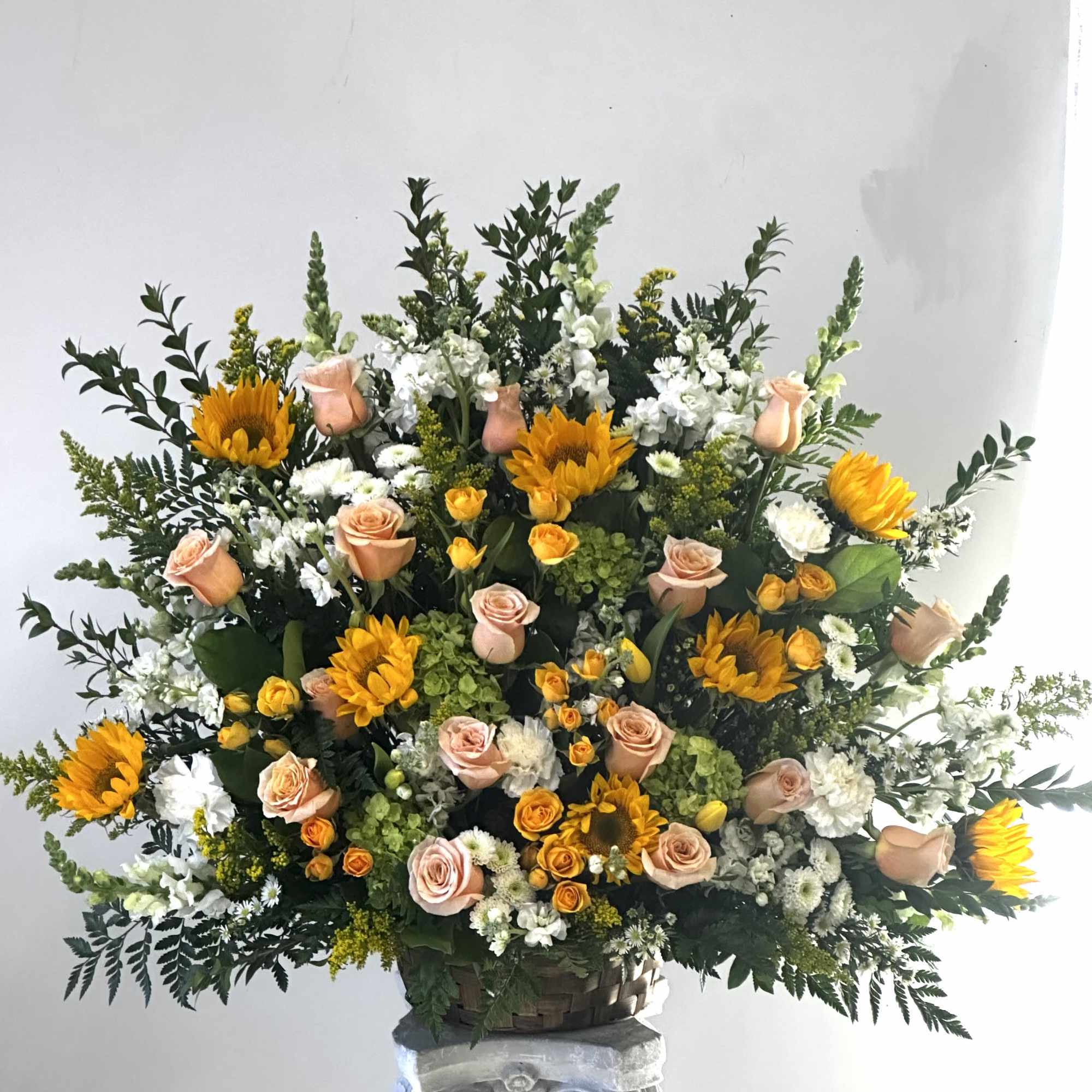 Large basket arrangement with peach roses, yellow sunflowers, and white flowers