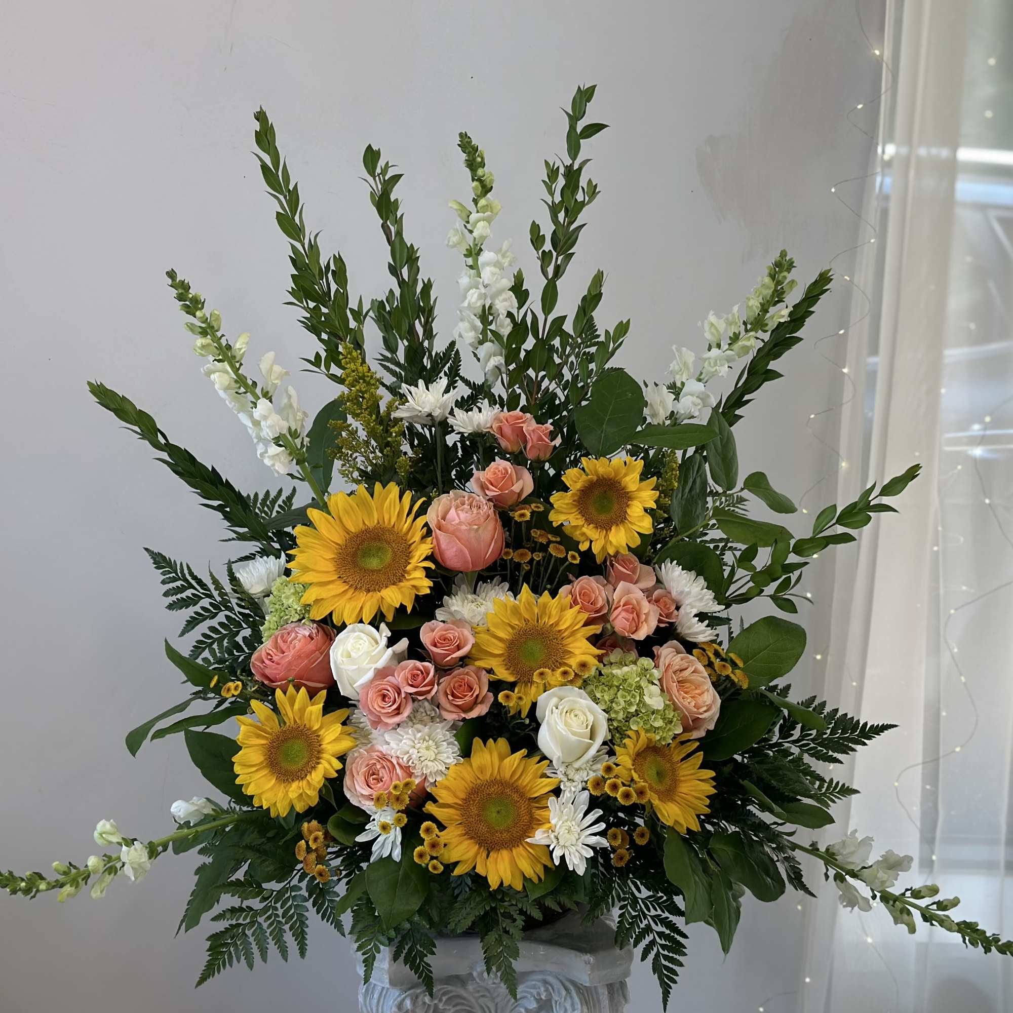 Large floral arrangement with sunflowers, roses, and white blooms in a pedestal vase