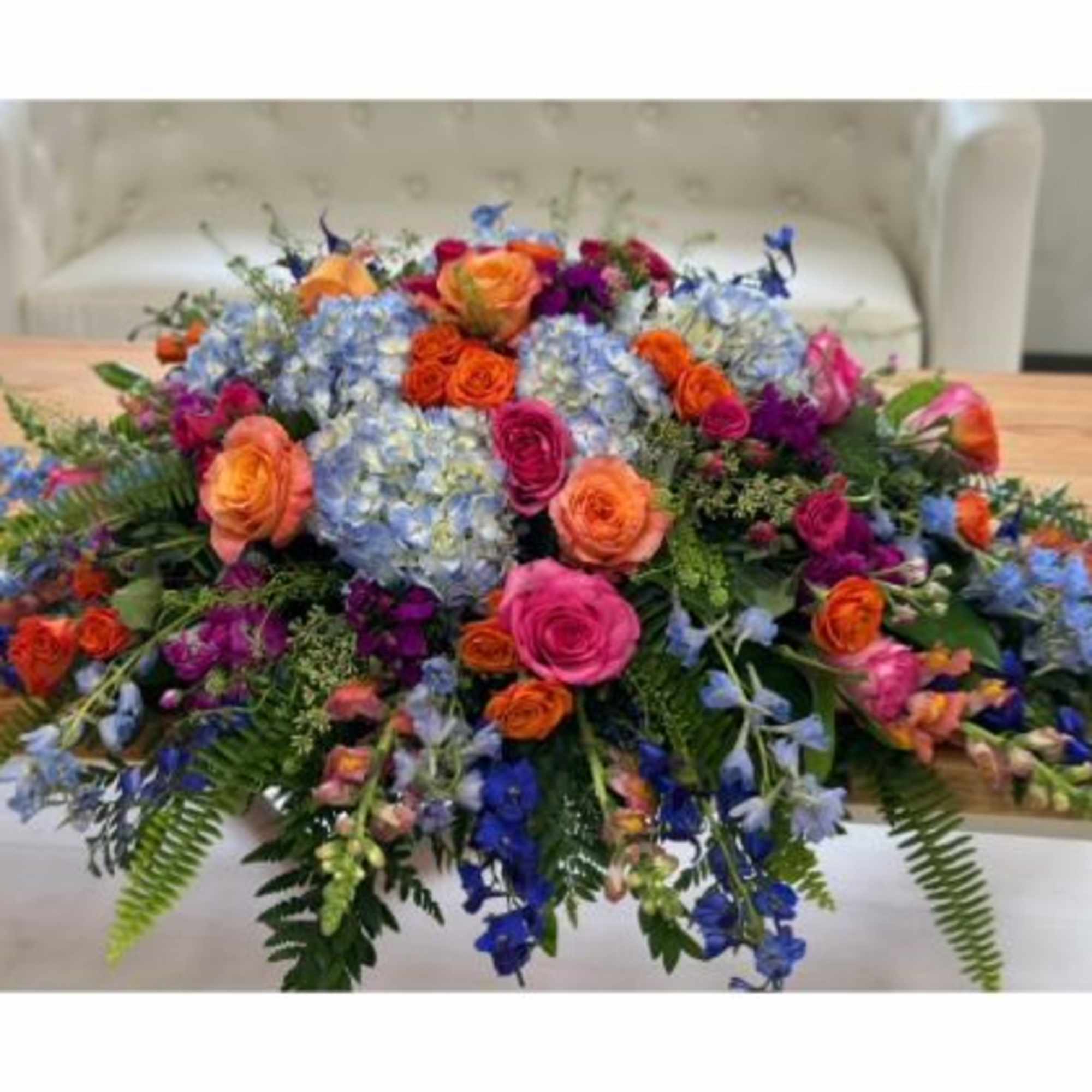 Large colorful floral centerpiece with roses and blue hydrangeas on a table