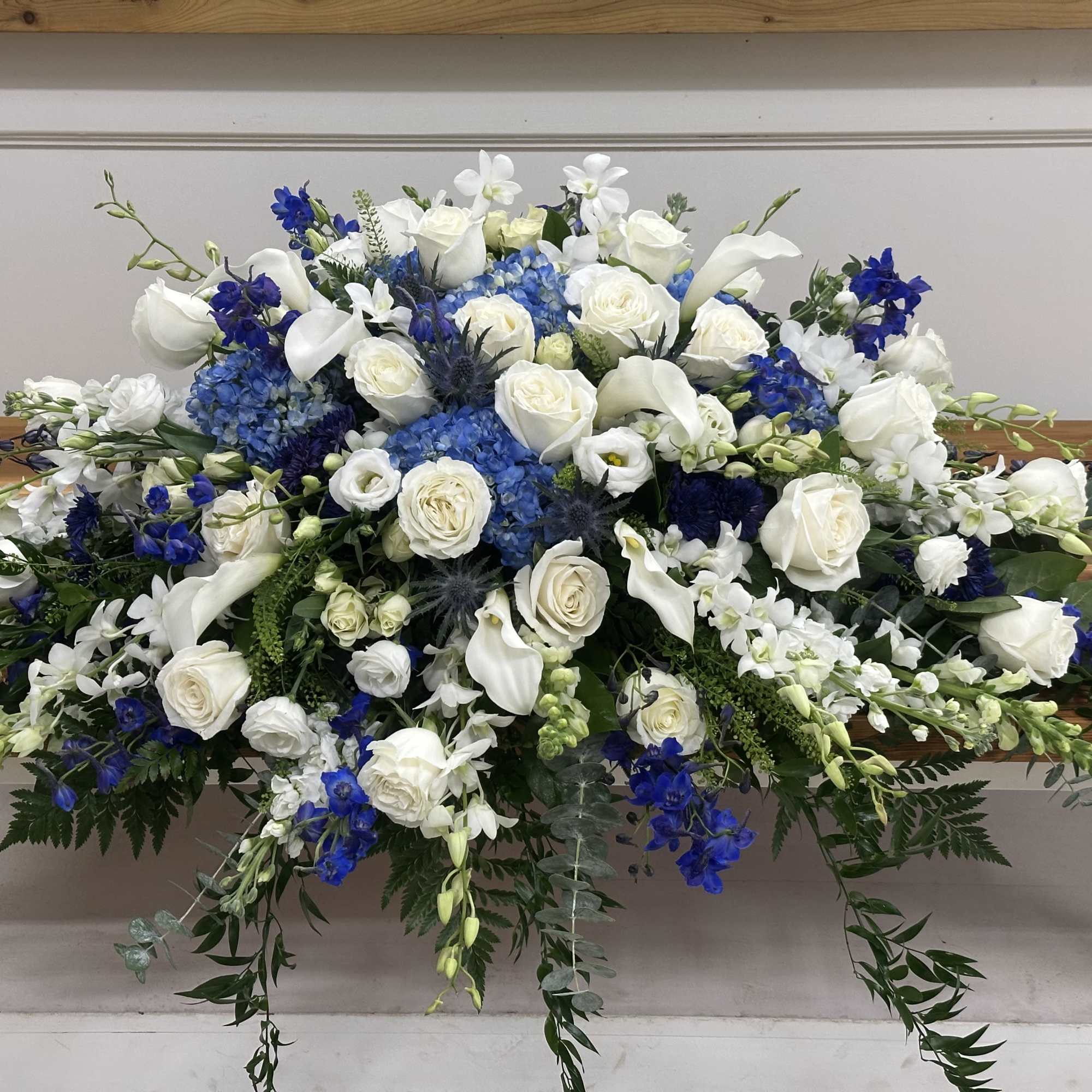 Large white and blue floral arrangement on a wooden casket