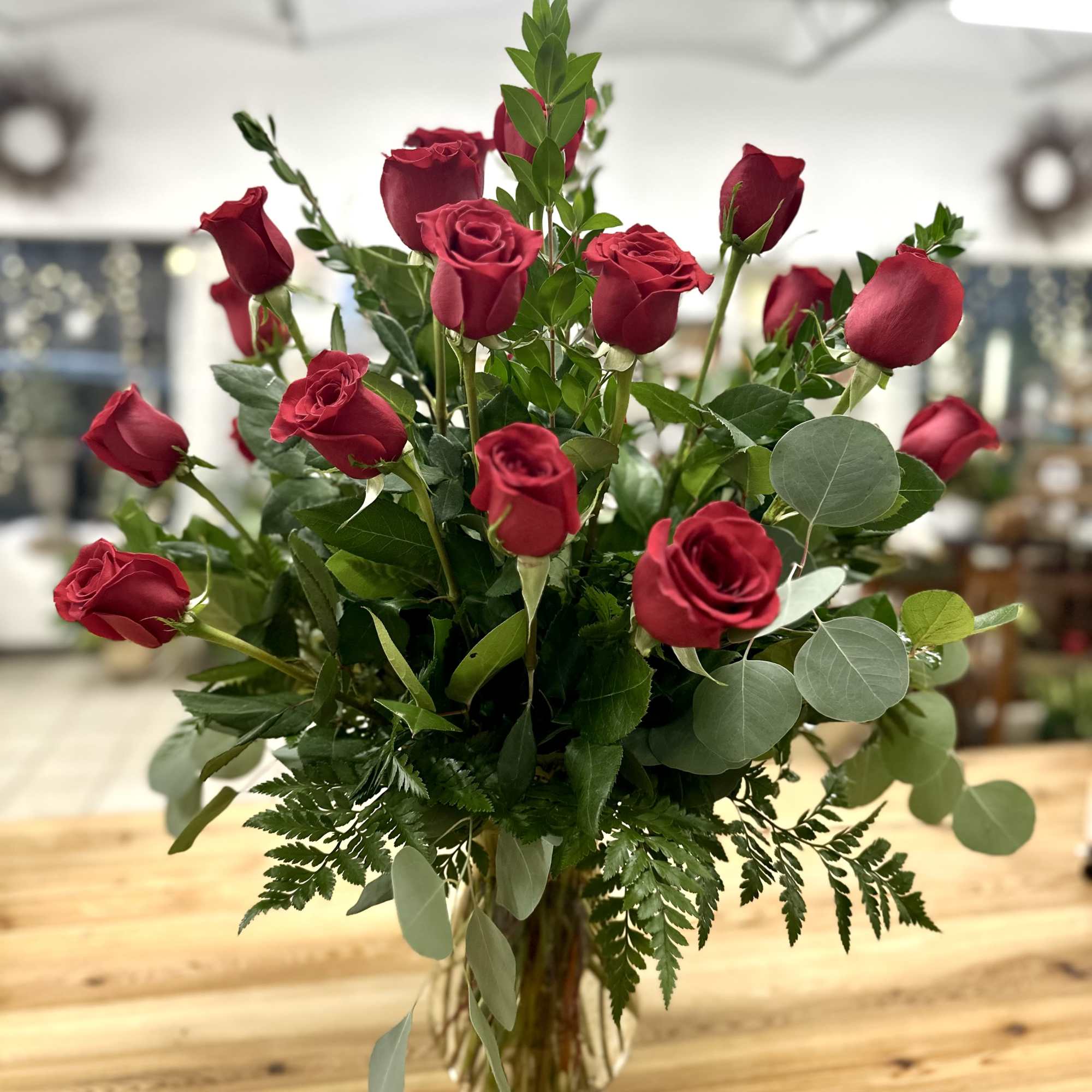 Red roses arranged in a clear glass vase with mixed greenery, photo 2 of 2