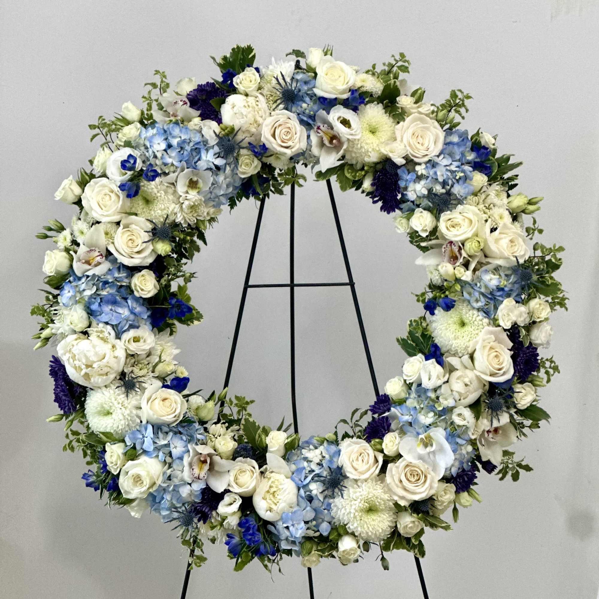Large floral wreath of white, blue, and purple flowers on a black stand