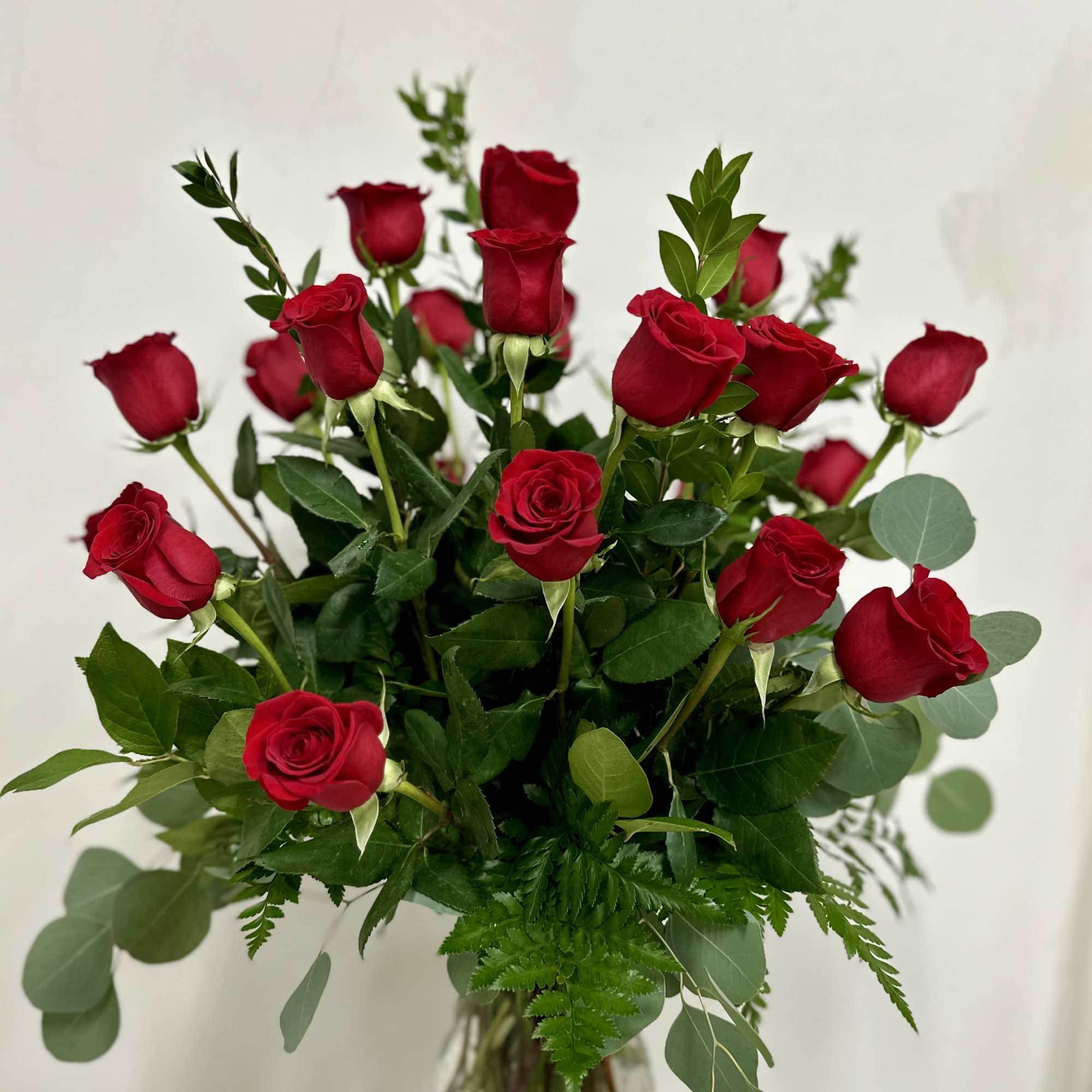 Red roses arranged in a clear glass vase with mixed greenery