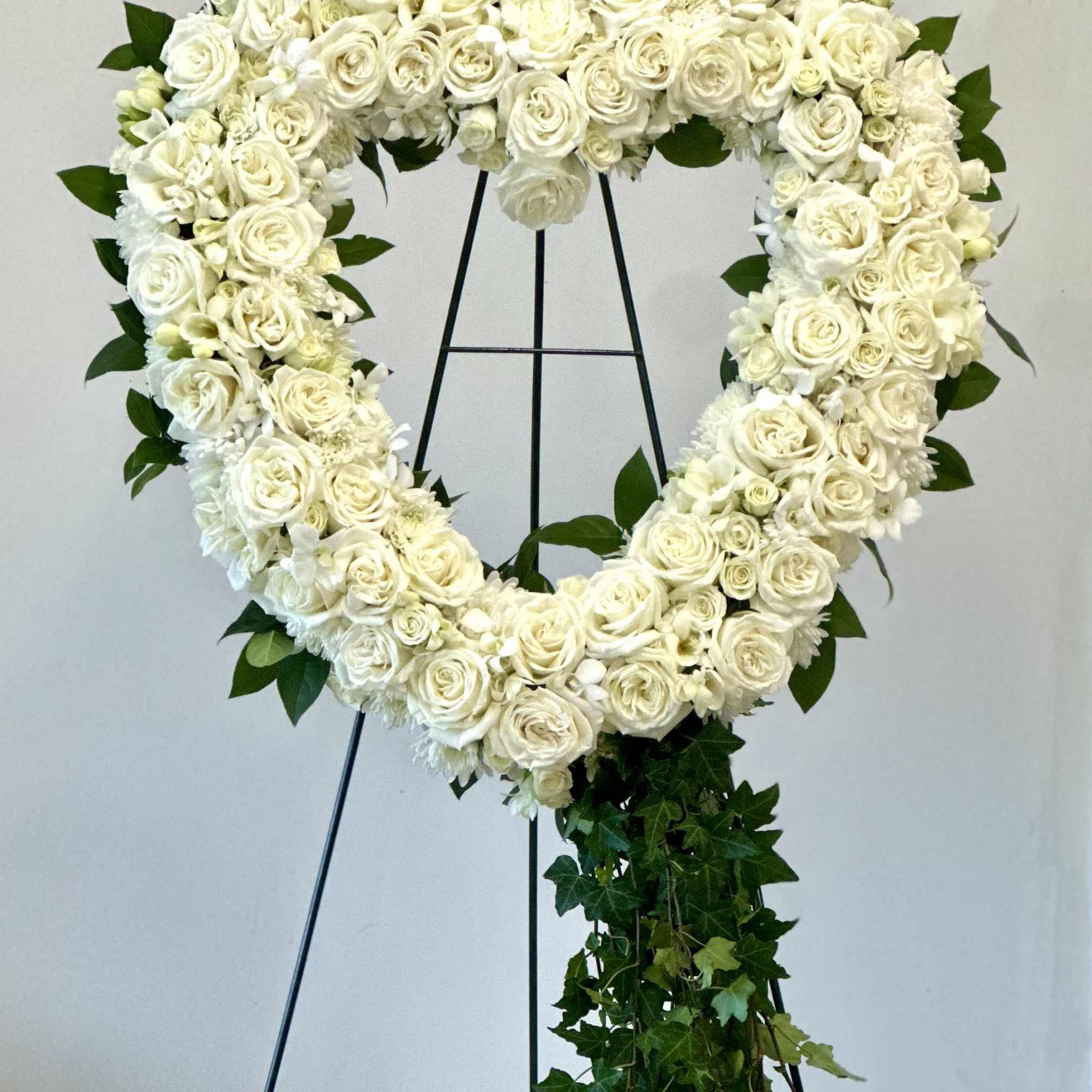 Heart-shaped white floral wreath on a stand with trailing ivy