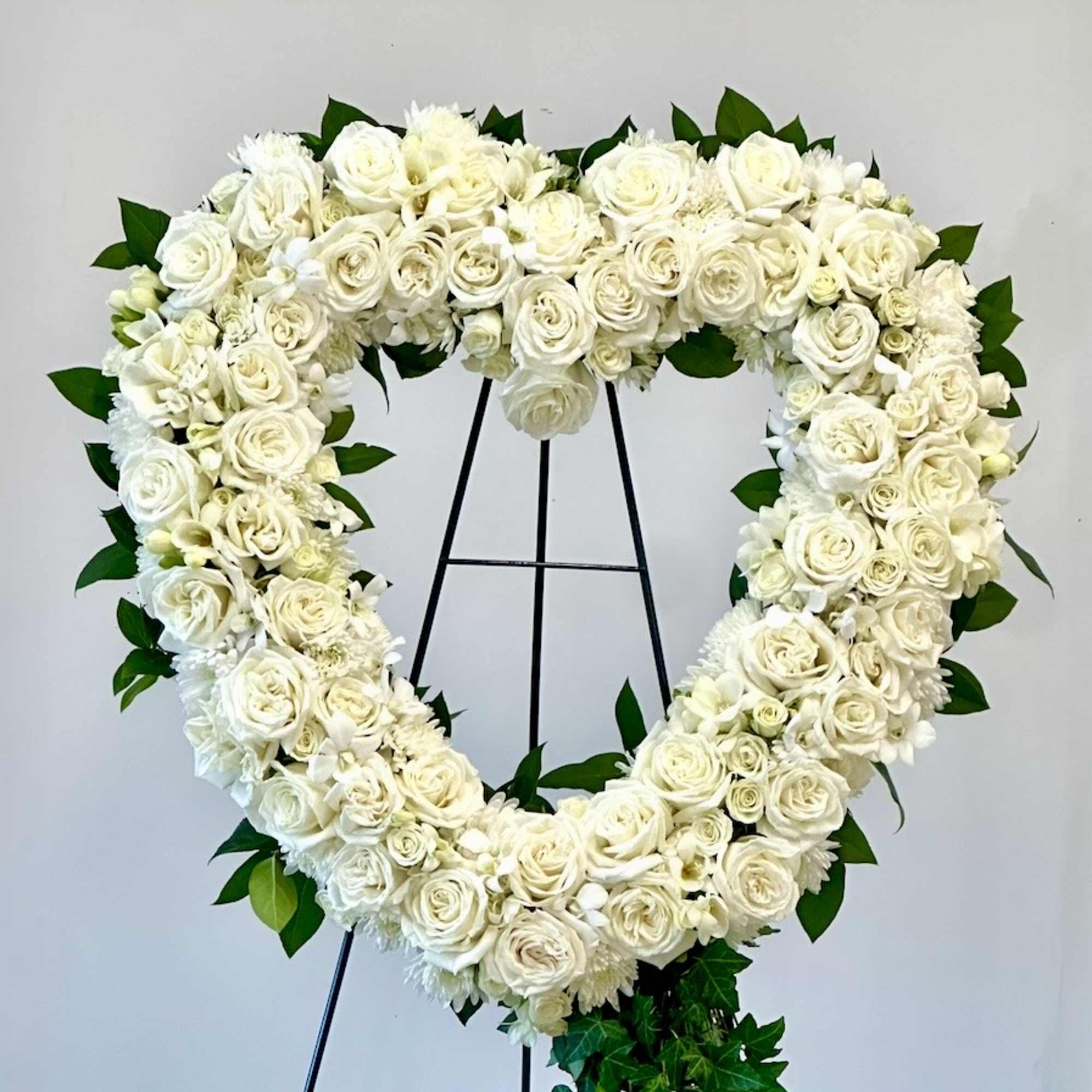 Heart-shaped white rose floral wreath on a black stand
