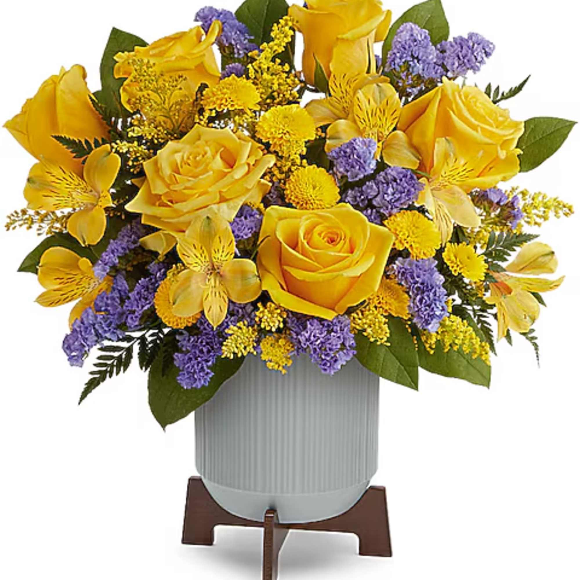 Yellow roses and purple filler flowers in a white vase on a stand