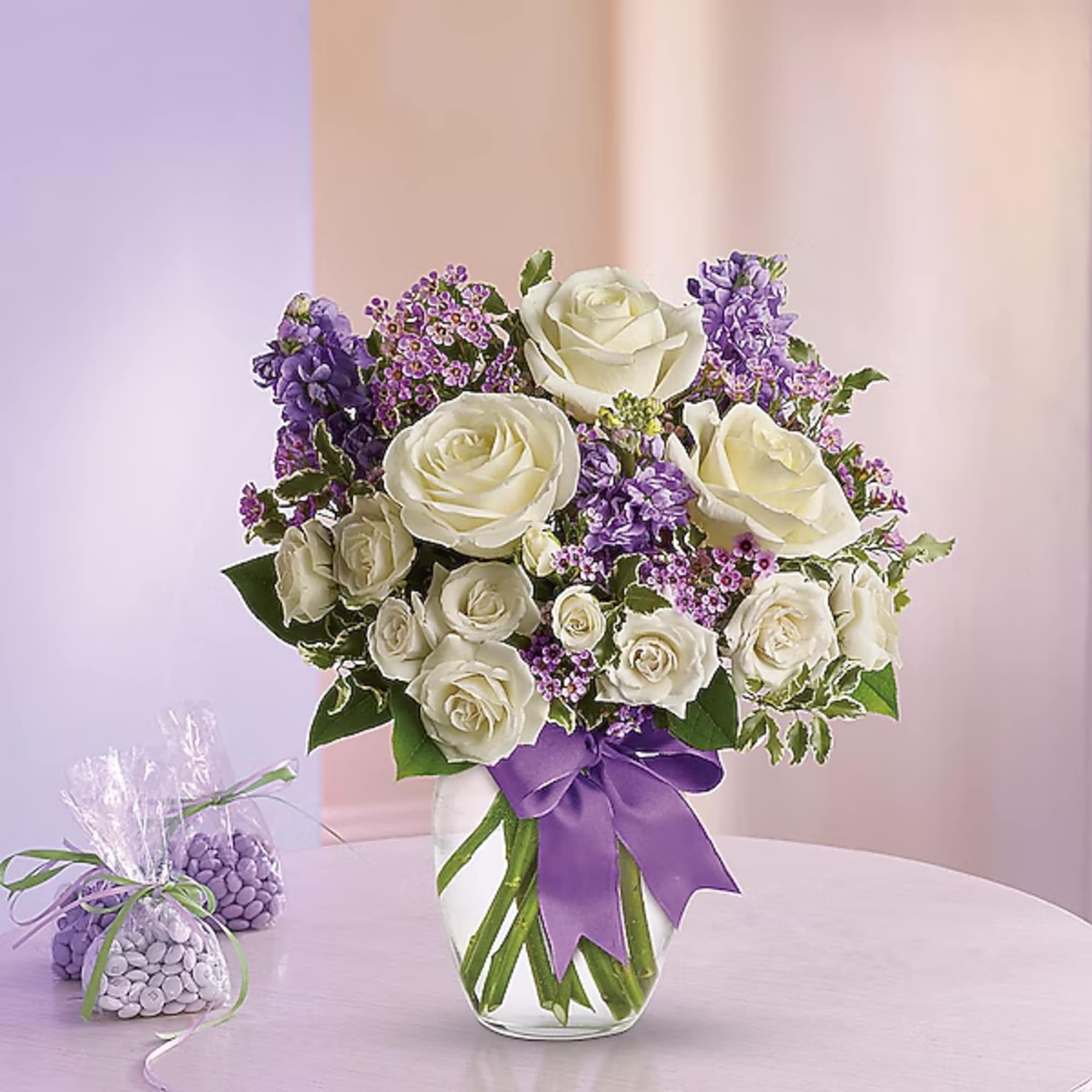 White roses and purple flowers in a glass vase with a purple ribbon