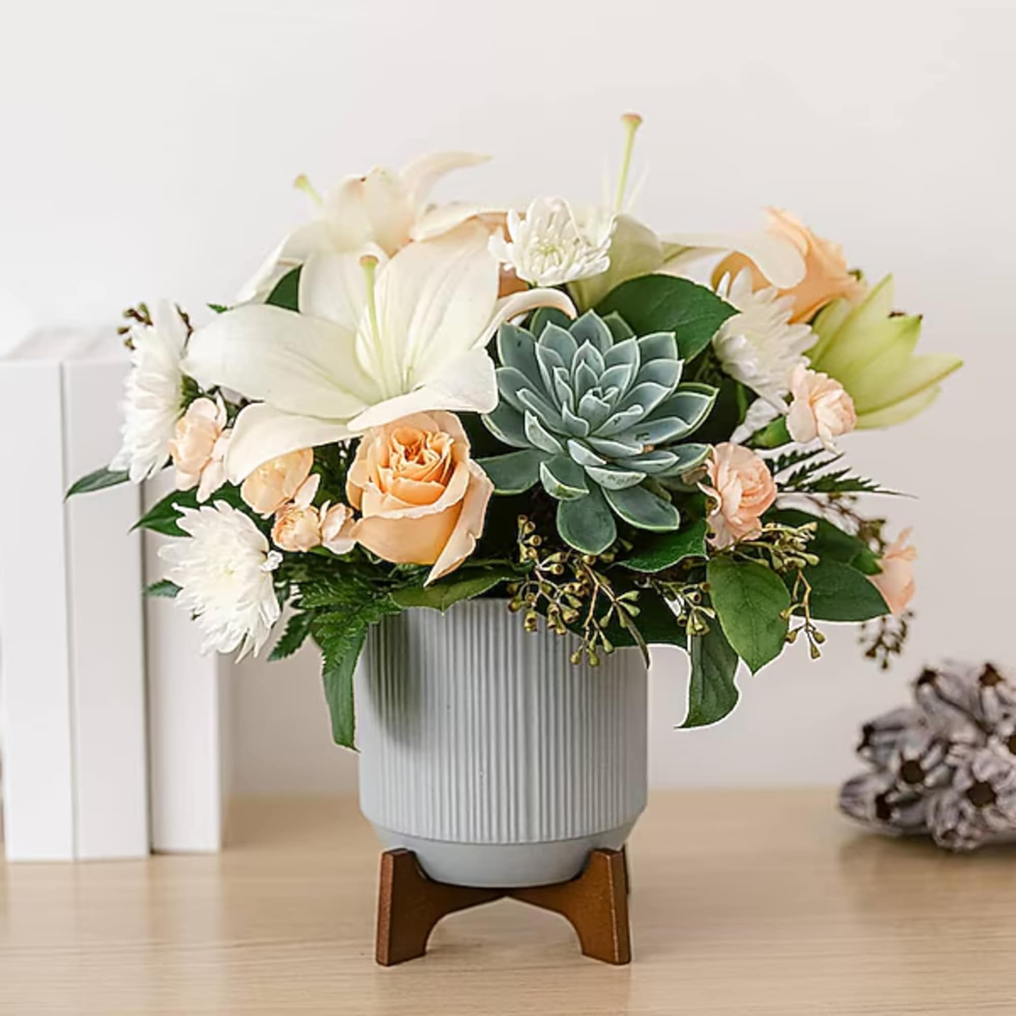 Arrangement of white lilies, peach roses, and a succulent in a ribbed vase