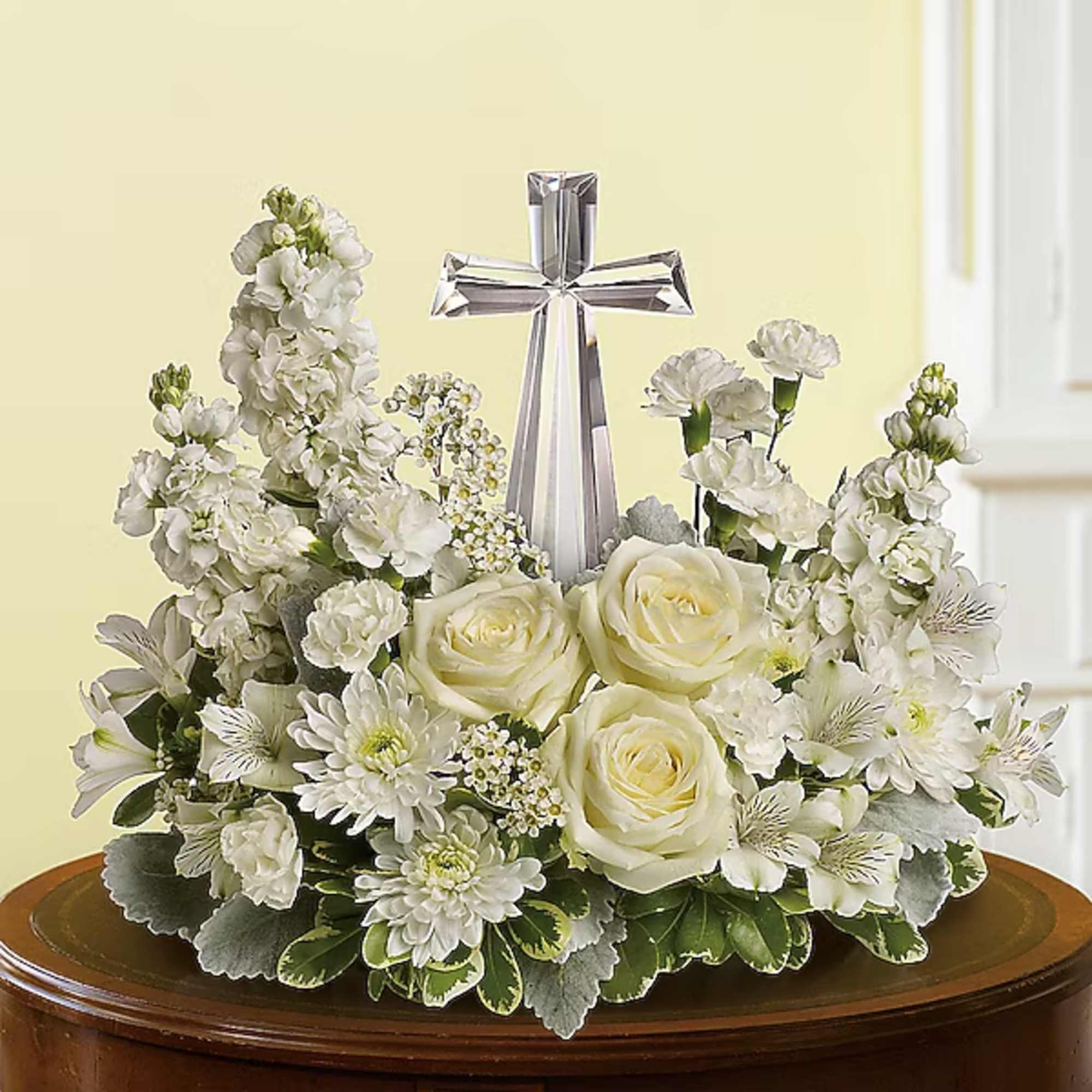 White floral arrangement with roses, daisies, and a silver cross centerpiece