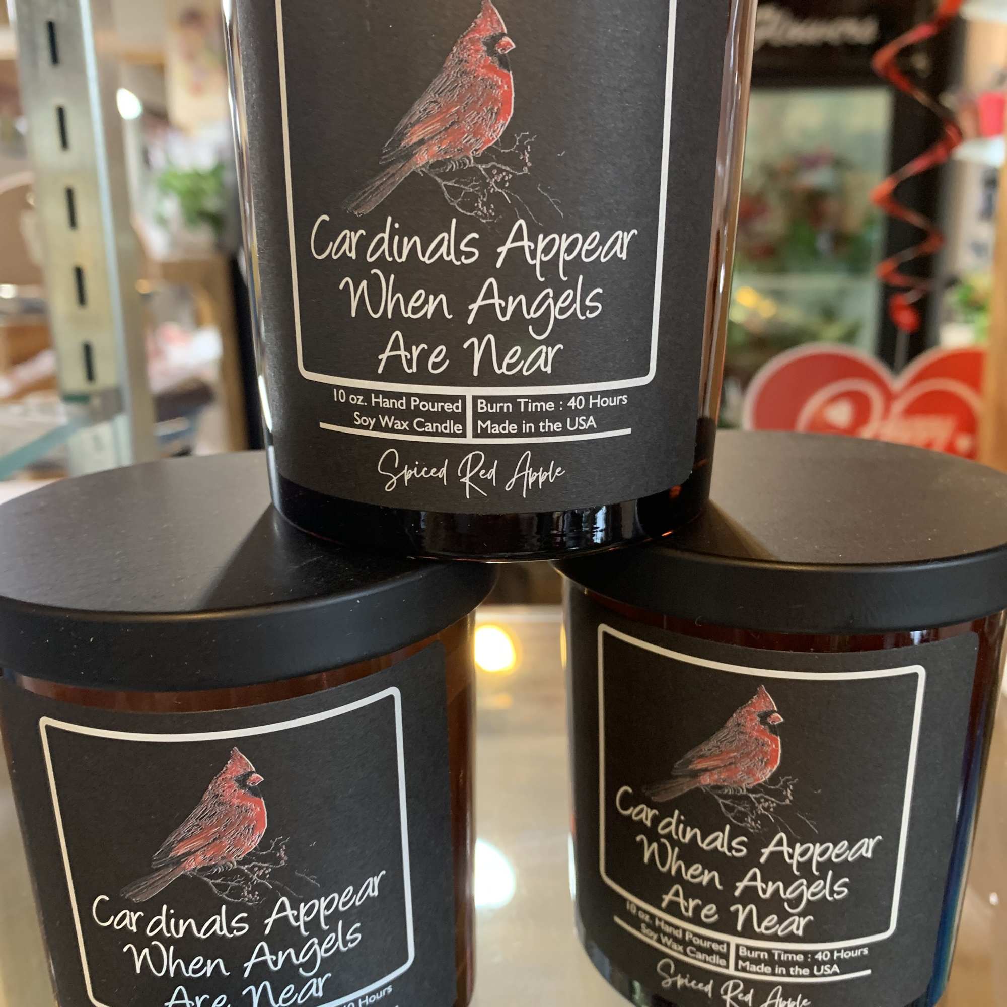 Three black-lidded candles with cardinal labels and memorial text