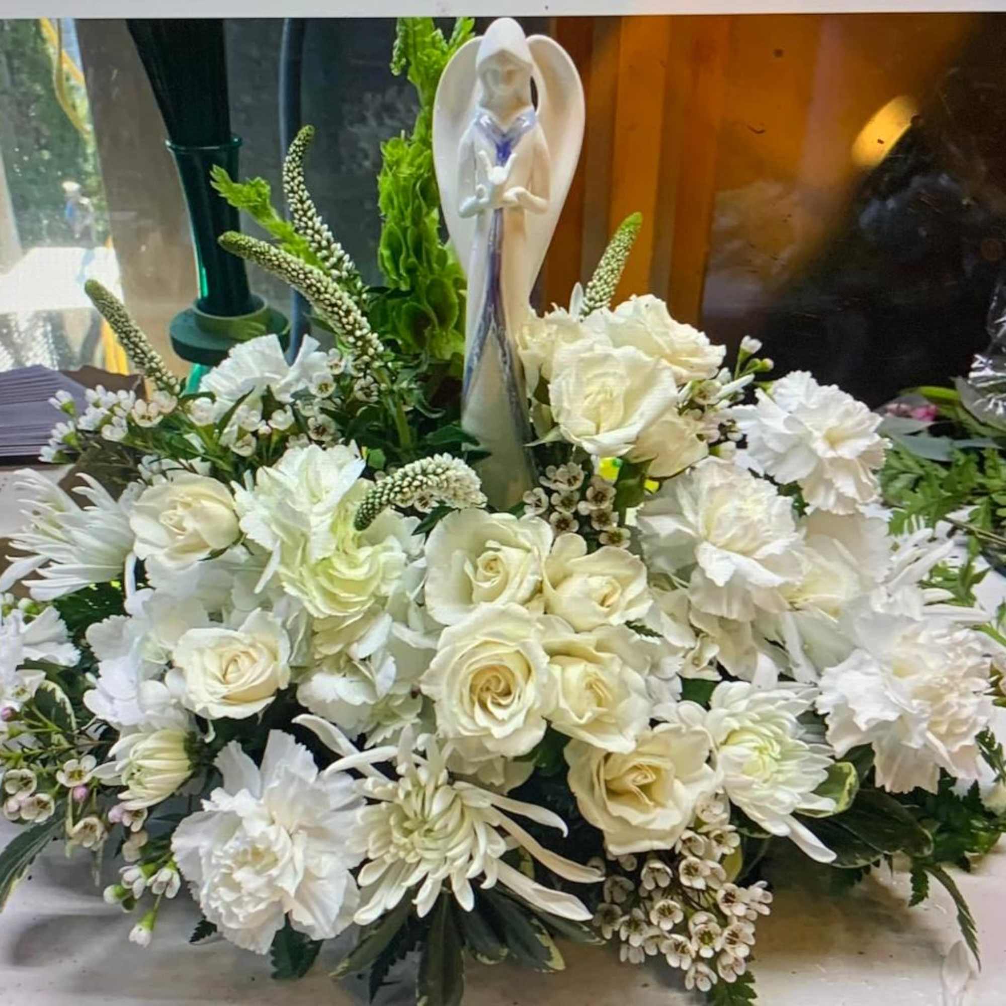 White floral arrangement with roses and carnations around a figurine centerpiece