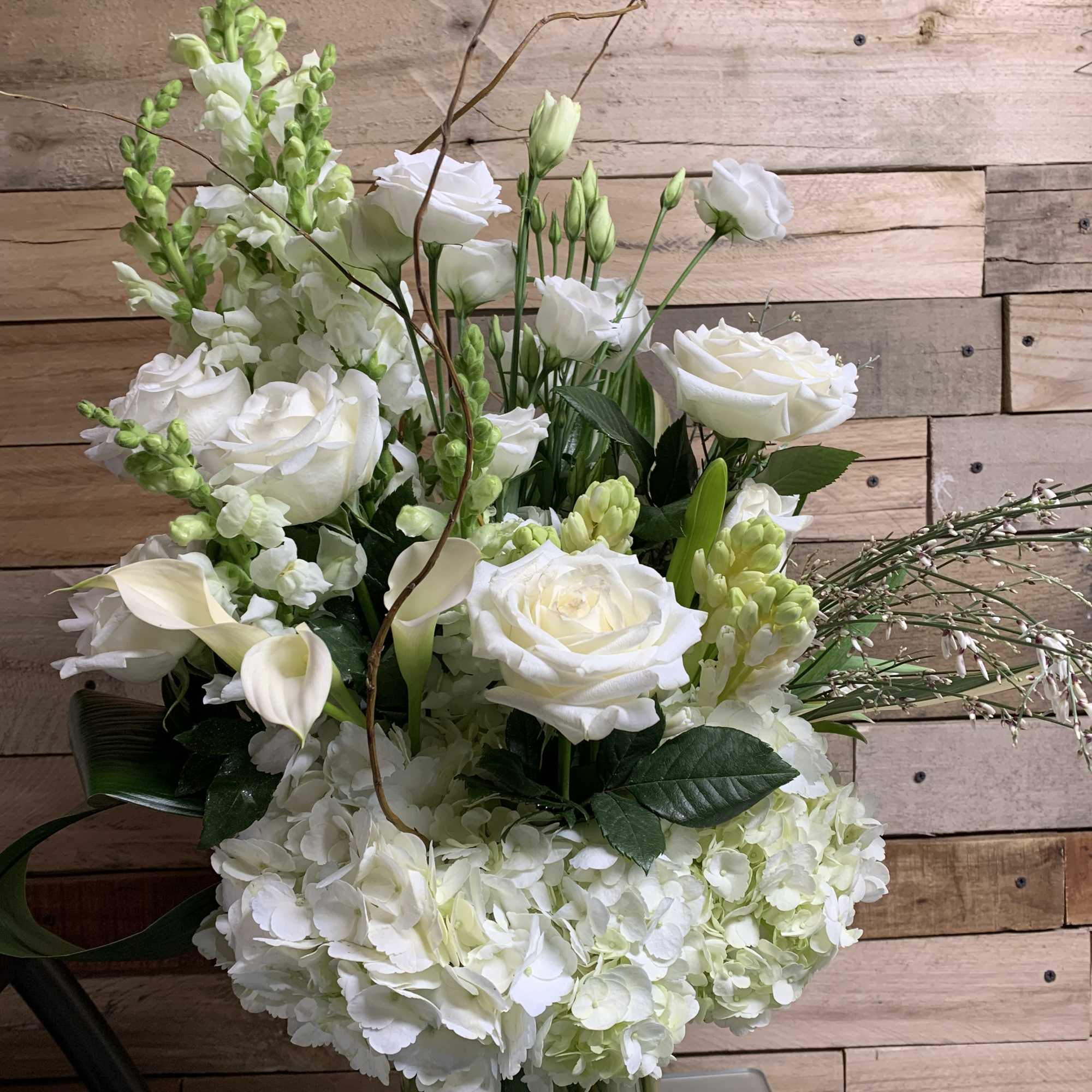 White floral arrangement with roses, hydrangeas, calla lilies, and snapdragons in a glass vase
