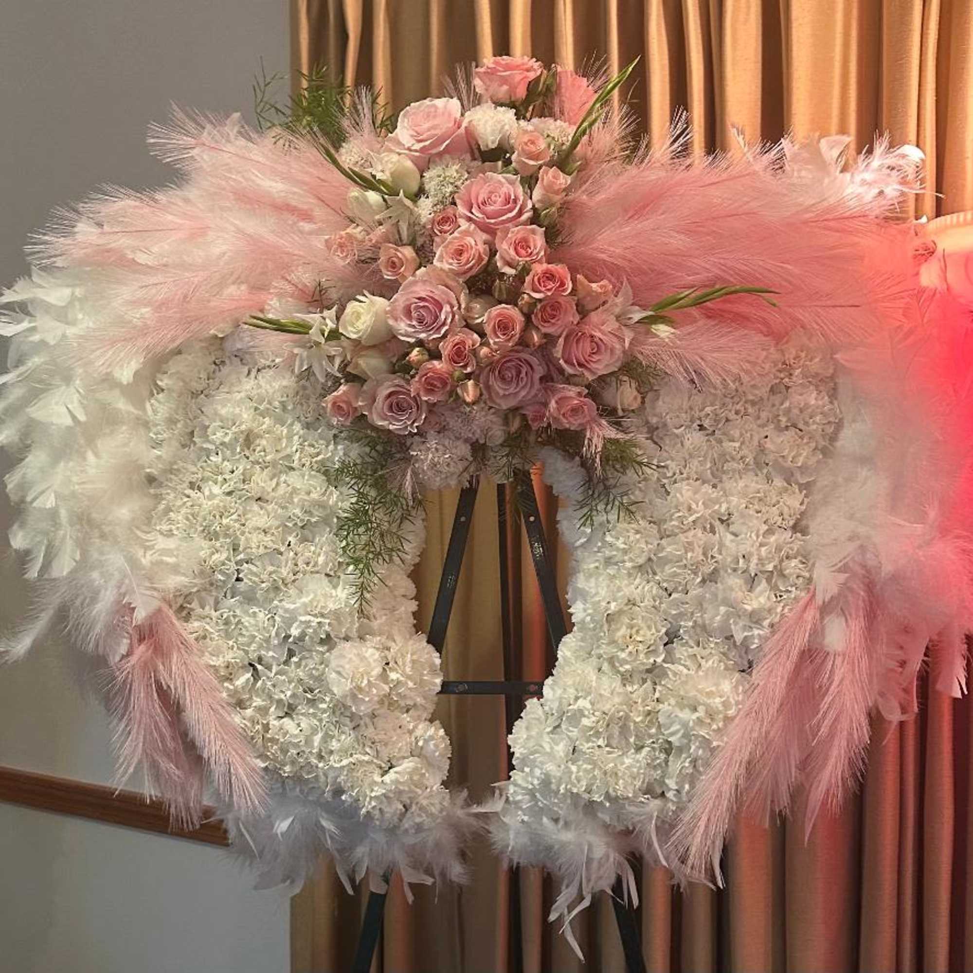 Pink and white floral wreath on an easel with feather accents