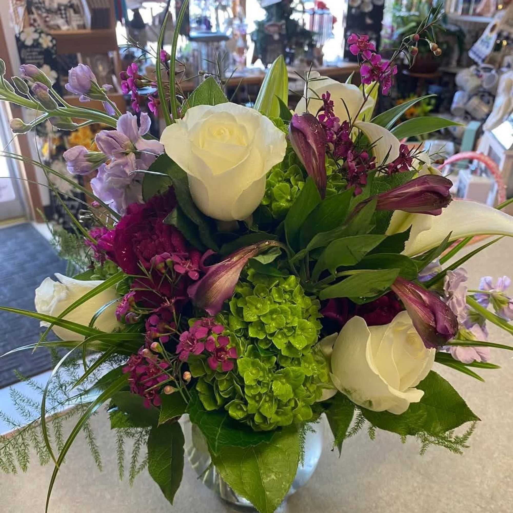 Bouquet of white roses, purple flowers, and green hydrangeas in a glass vase