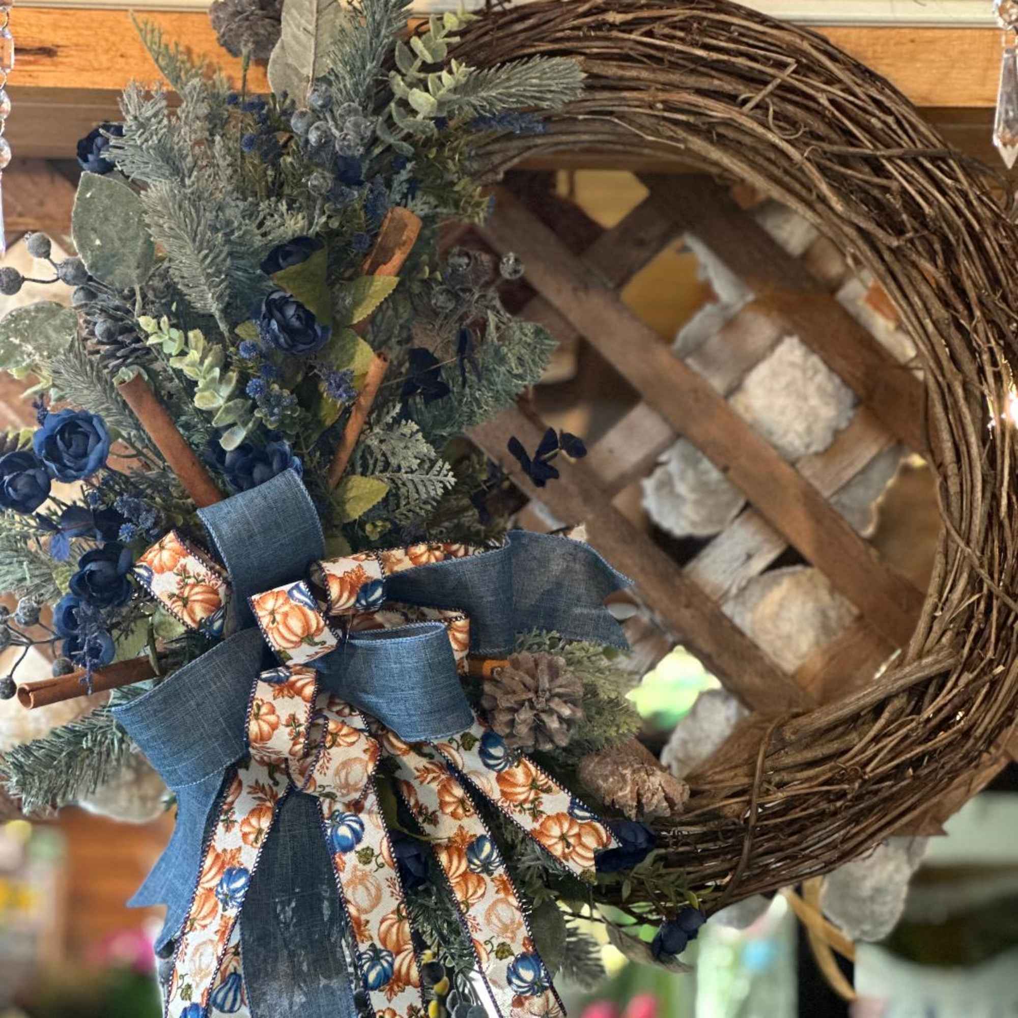 Rustic grapevine wreath with blue roses, evergreen sprigs, pinecones, and denim and pumpkin-print ribbons