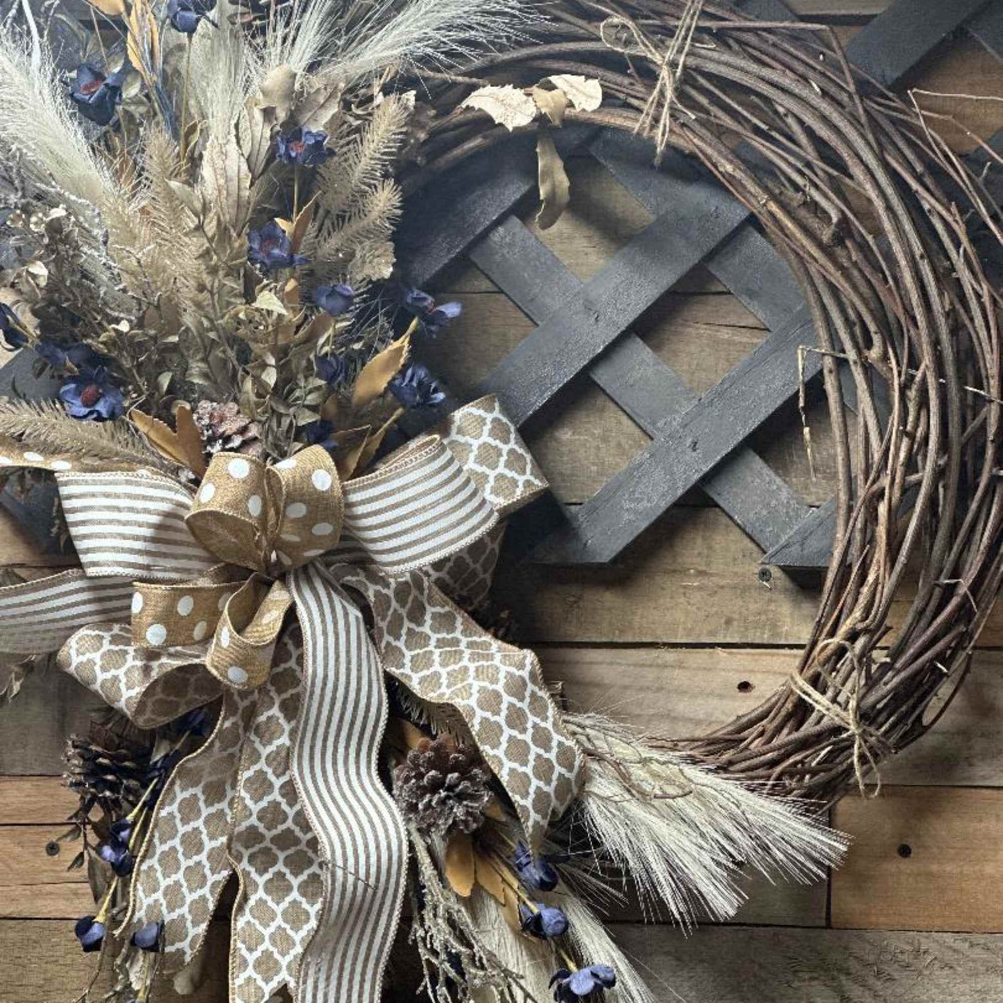 Rustic grapevine wreath with dried grasses, navy accent flowers, pinecones, and a large patterned ribbon bow