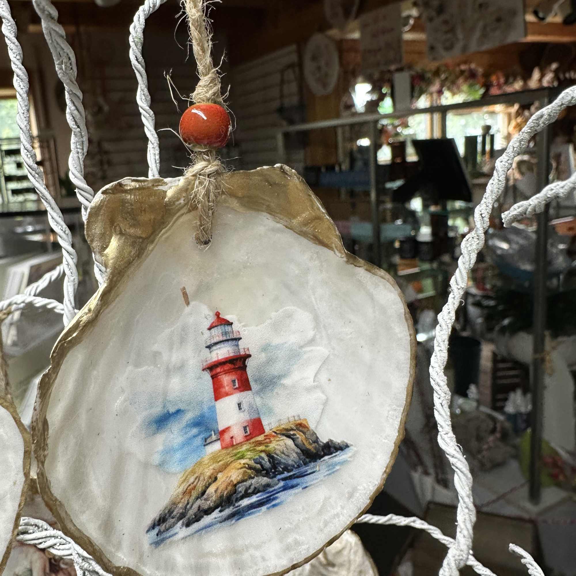 Round shell ornament with a painted lighthouse hanging by rope