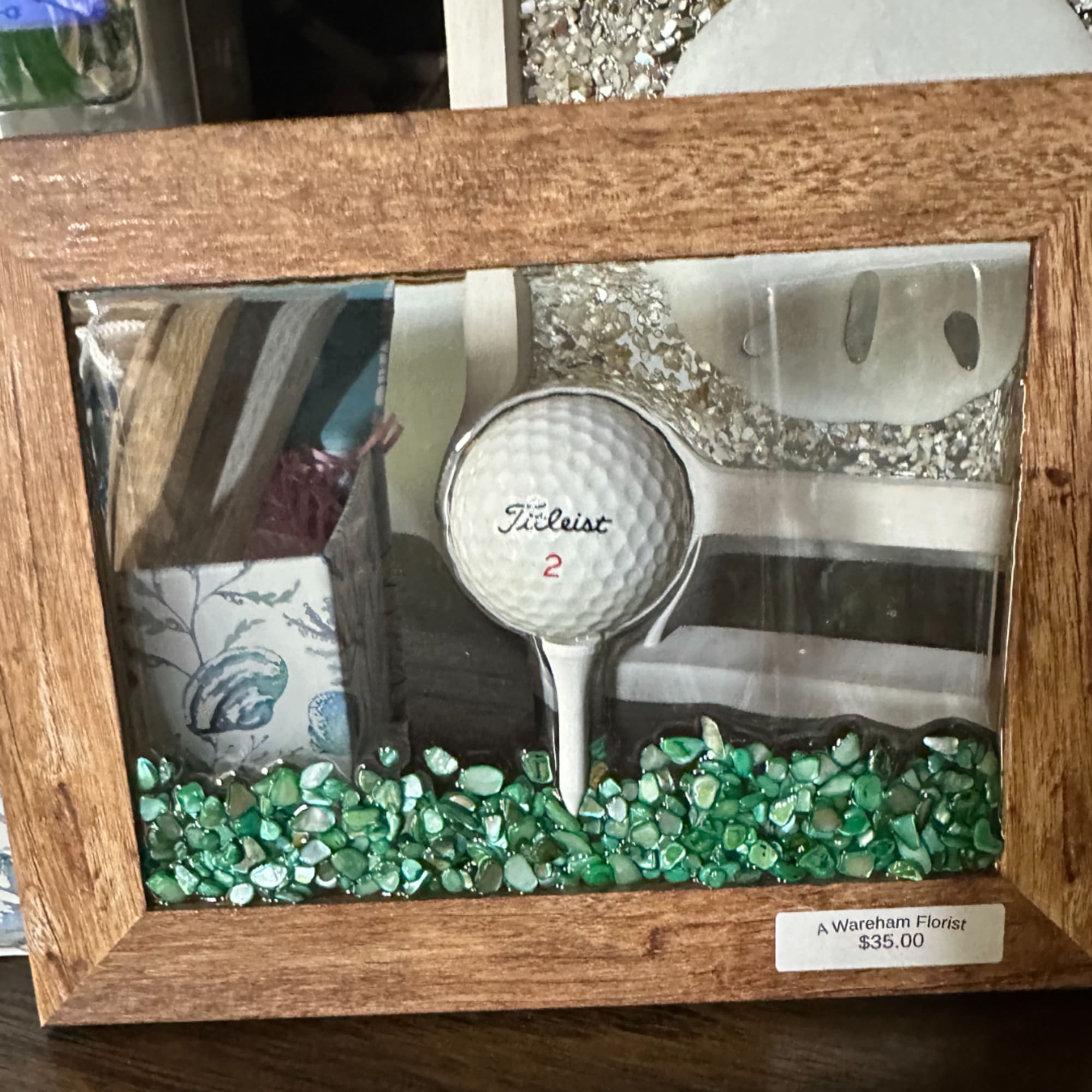Framed golf-themed shadow box with a Titleist golf ball and green stones
