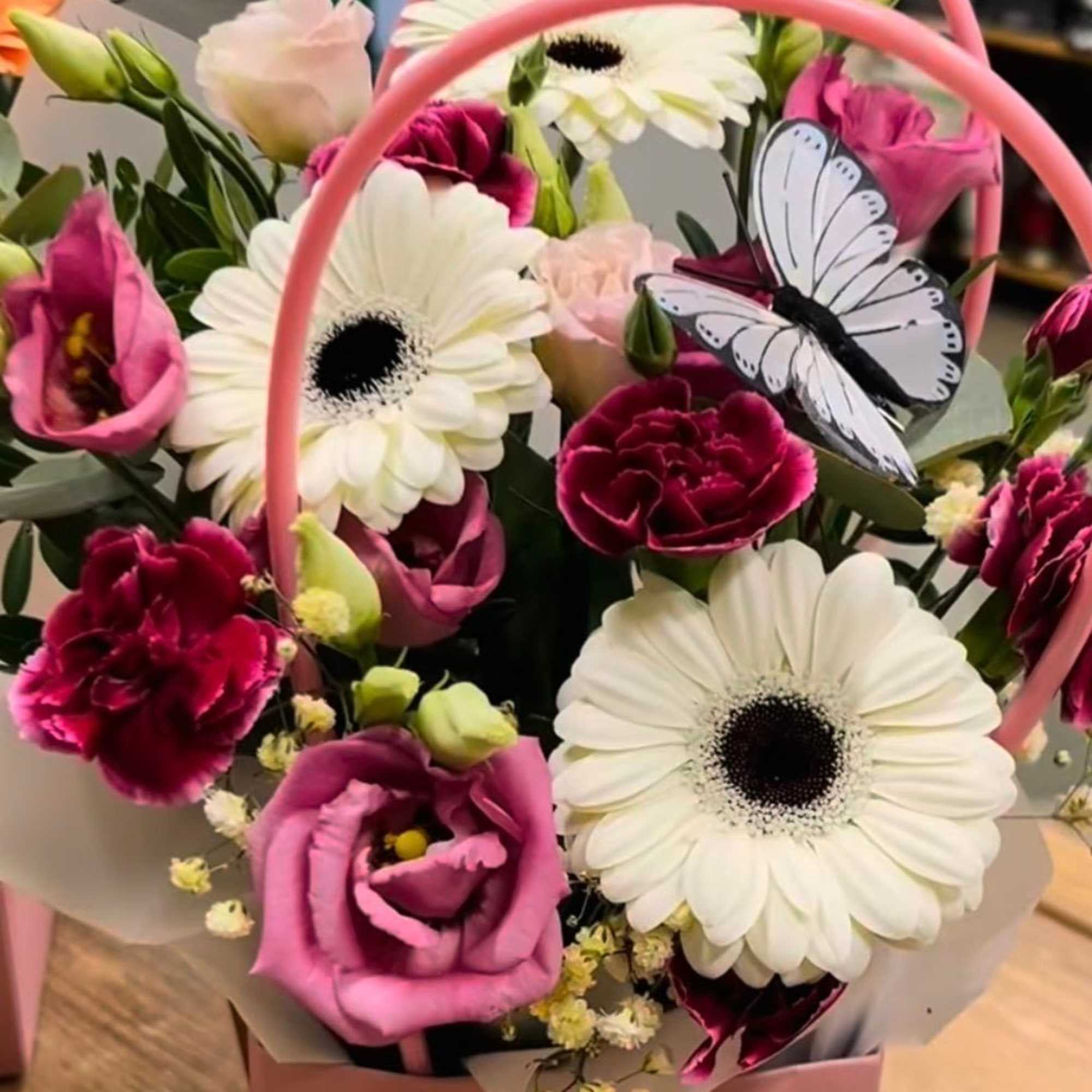 Pink and white mixed flower arrangement with gerbera daisies and carnations in a pink handled box with a butterfly decoration.